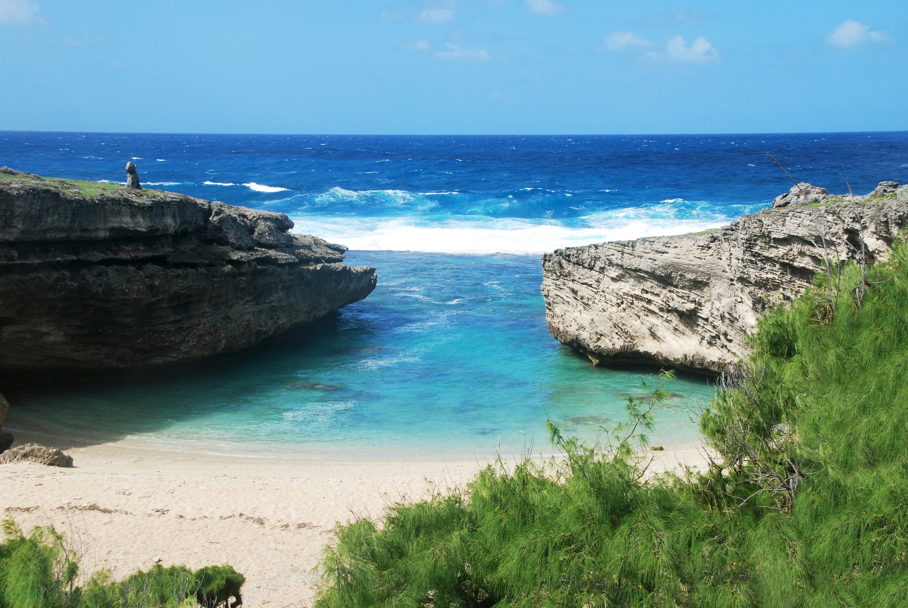 Two large rocks frame a beach cove. White waves are seen breaking beyond the rocks.