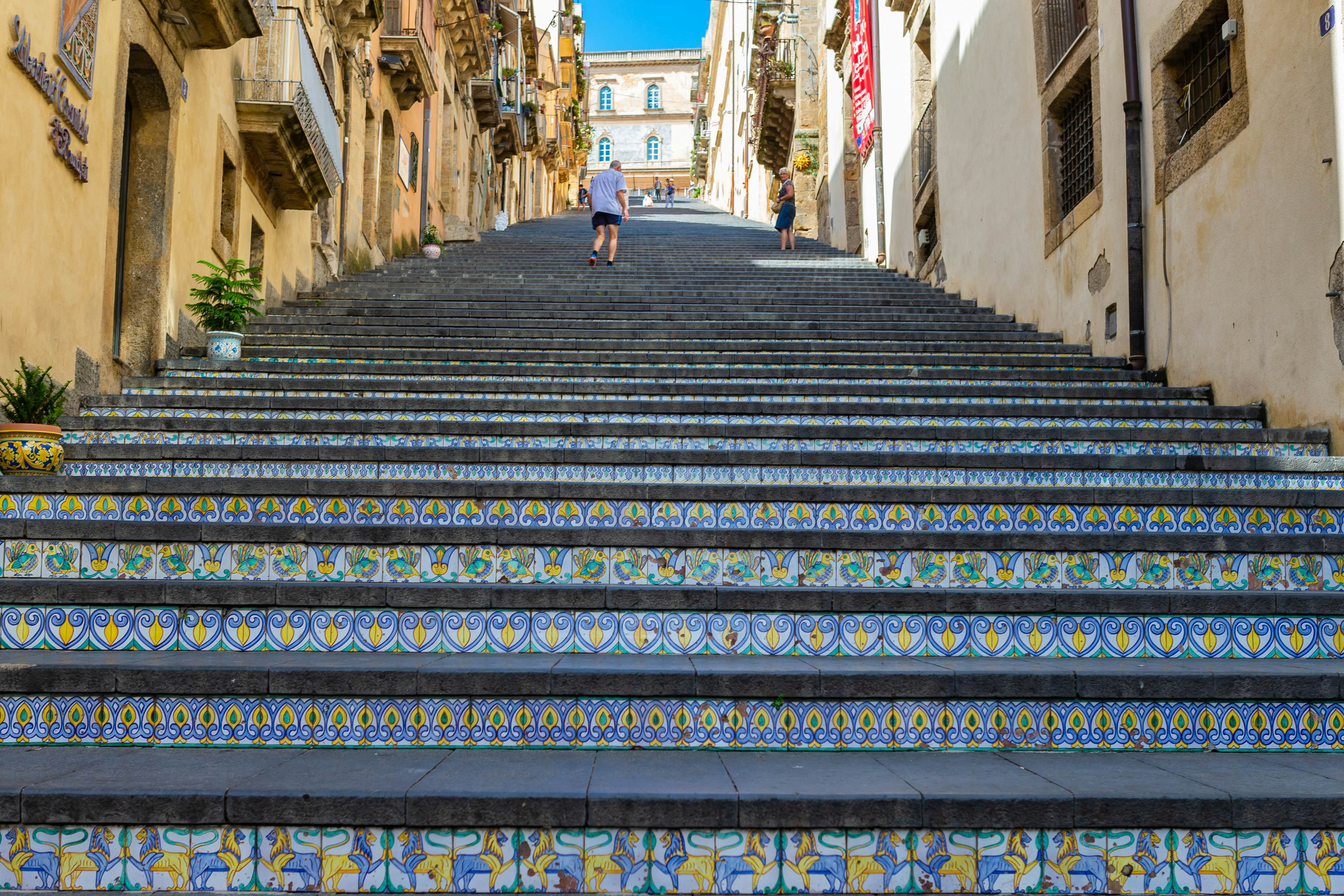 A man ascends a narrow outdoor staircase with colorful tiles on its risers in a historic town