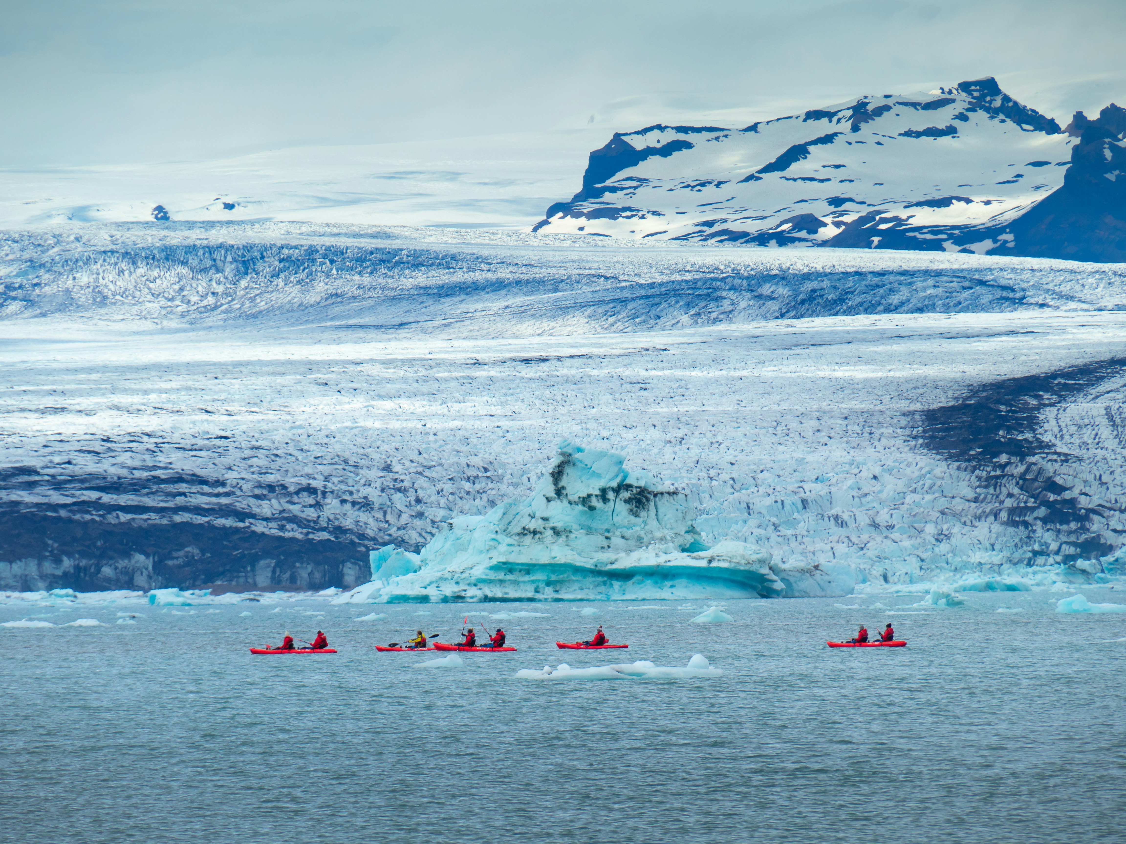 A wide shot of a group of people in red sea kayaks paddling past blue glaciers.