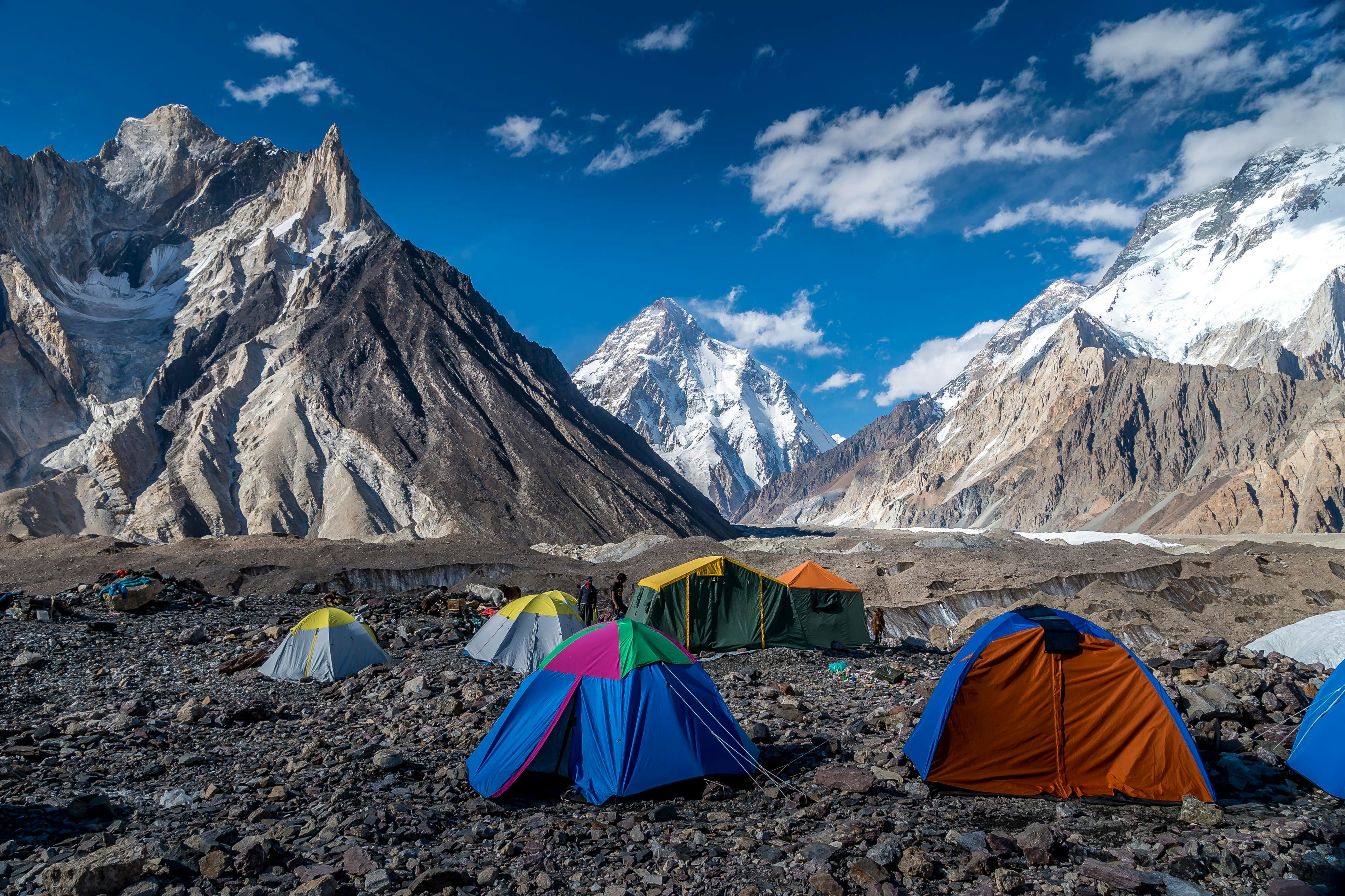 A series of two-person tents pitched on a rocky landscape with huge pointed mountains rising all around