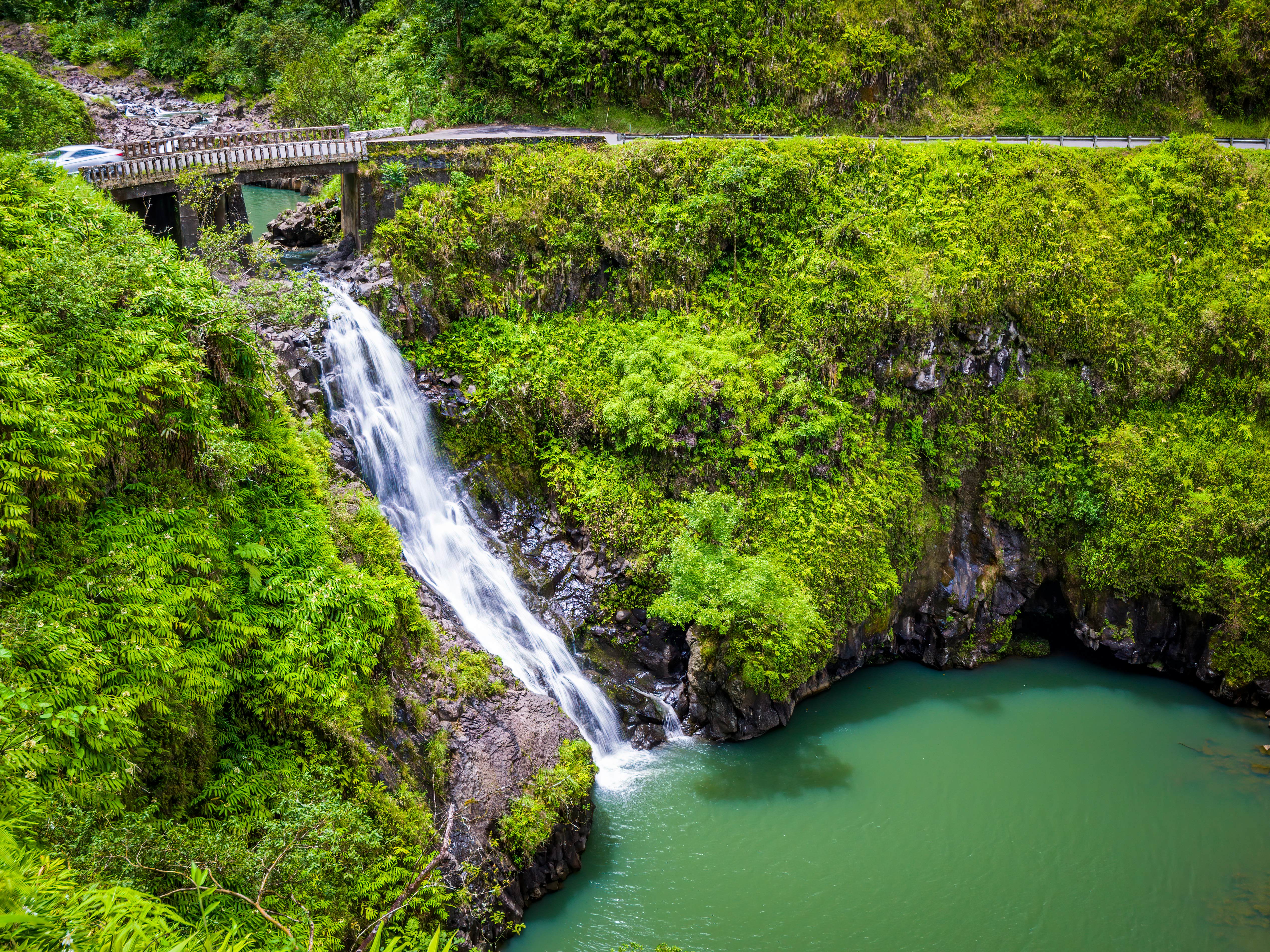 A car crosses a bridge over a waterfall on the Road to Hana in Maui