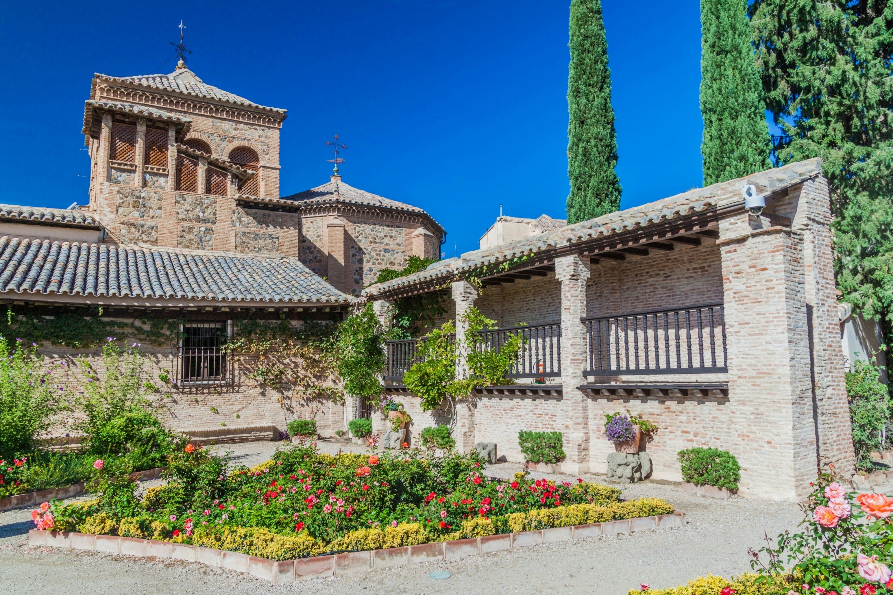 Exterior of a walled, stone house with plants and flowers displayed in its sunny courtyard