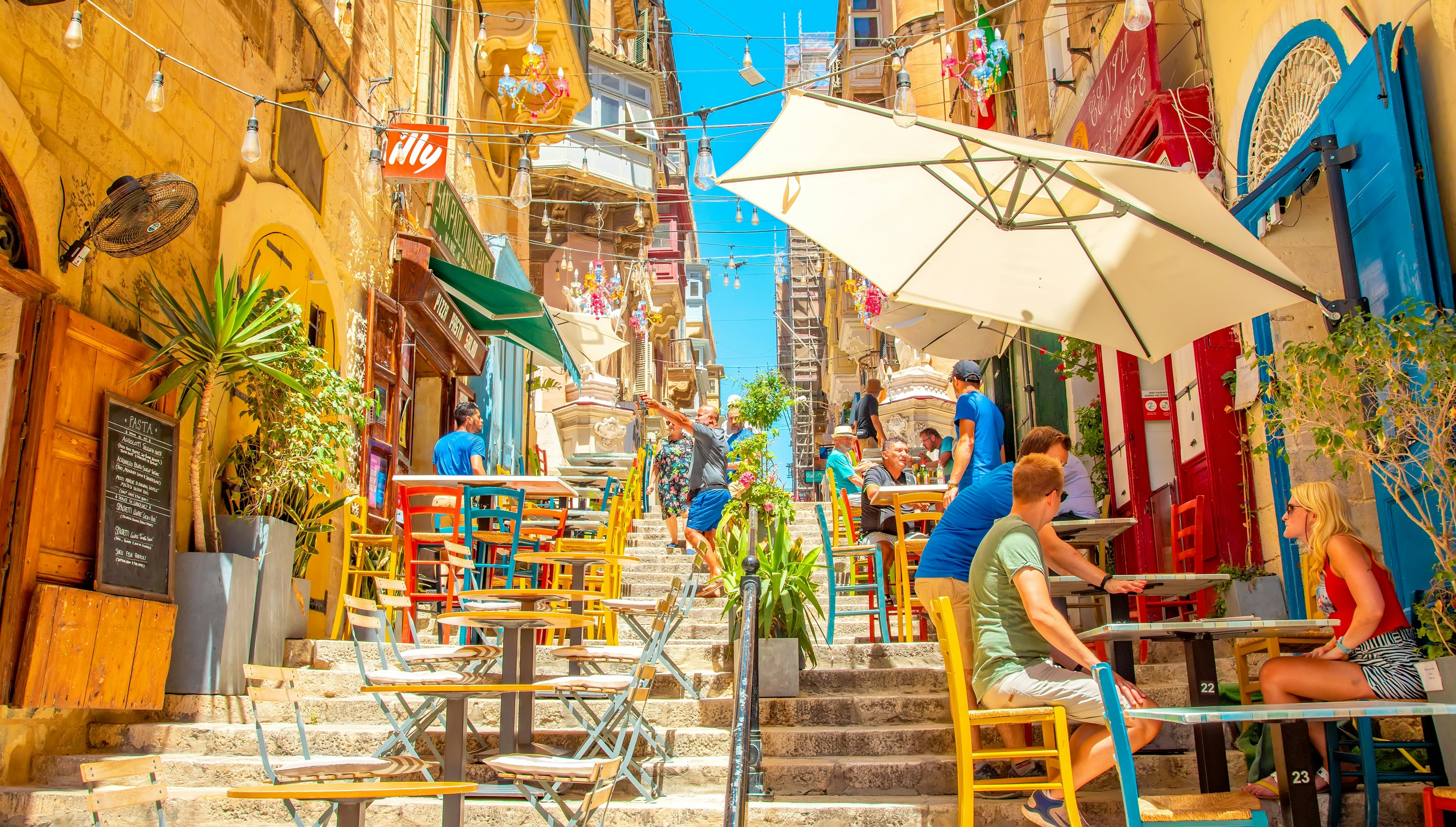 Wide panoramic view of summer street and pavement cafe in Valletta old town. Beautiful Maltese travel photo with colorful urban life.