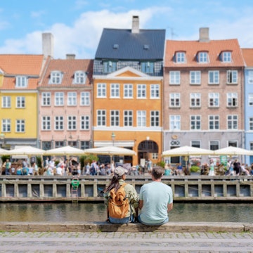 A couple sits on a stone wall overlooking a bustling Copenhagen canal, taking in the vibrant facade of historic buildings and the lively atmosphere of the waterfront. Copenhagen Denmark , License Type: media, Download Time: 2025-02-20T16:49:52.000Z, User: Ppeterson948, Editorial: false, purchase_order: 56530 - Guidebooks, job: Global Publishing WIP, client: Global Publishing WIP, other: Pia Peterson Haggarty