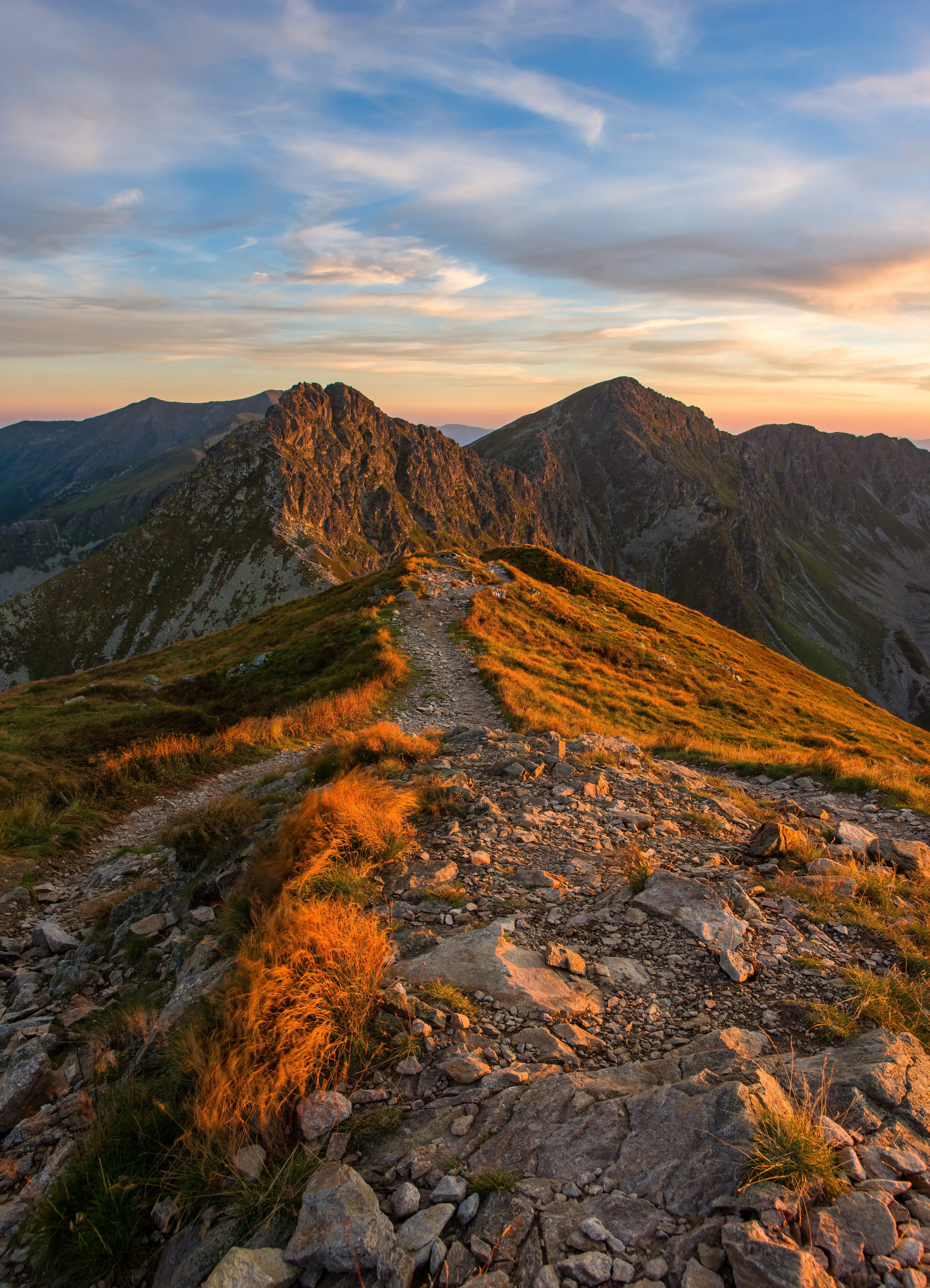 A trail on a mountain ridge, with autumn grass and a colorful sky.