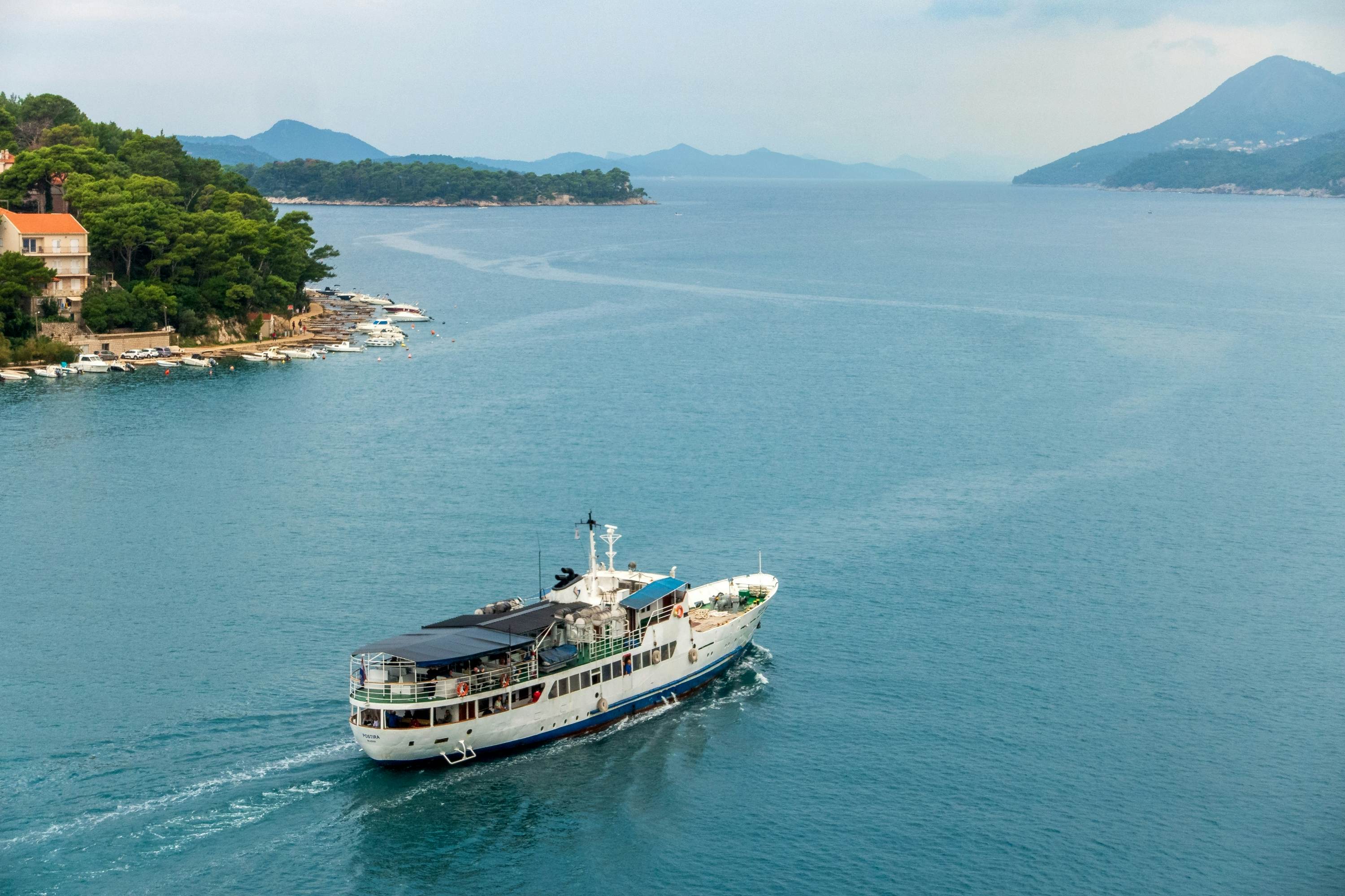 An aerial view of a passenger ferry moving between islands. Hills are visible on land in the distance.