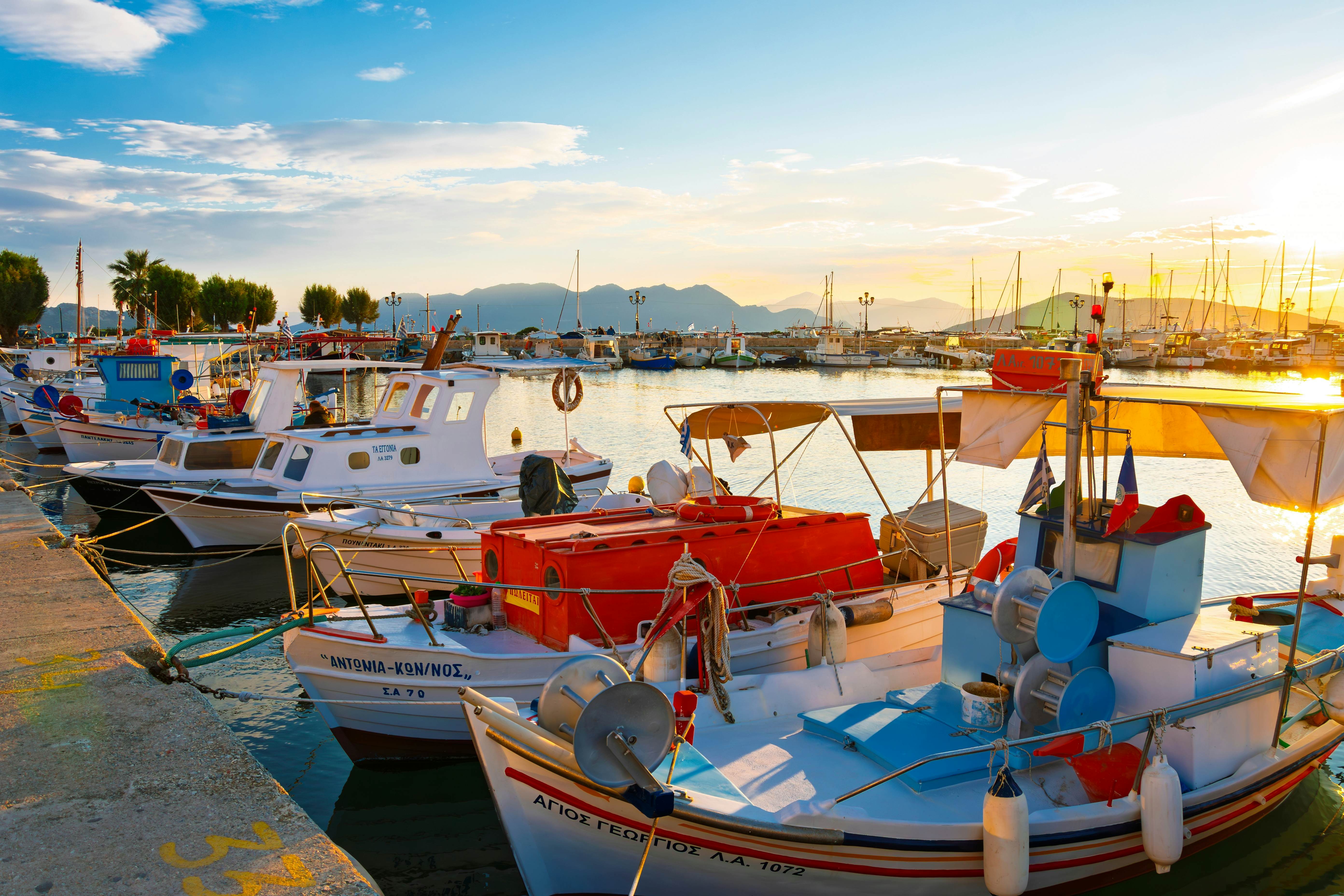 Boats are moored at a harbor, lit by dramatic light from the setting sun.