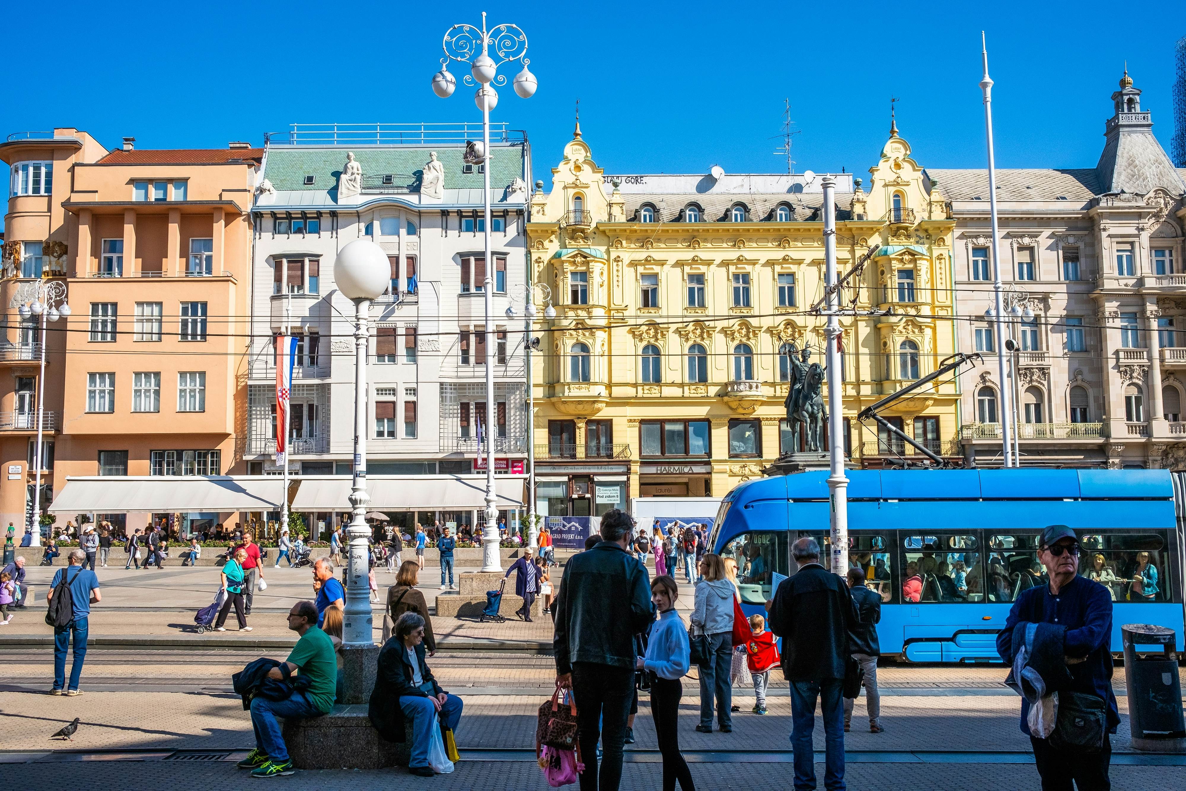 Historic buildings in pastel towns contrast against the blue tram in Zagreb