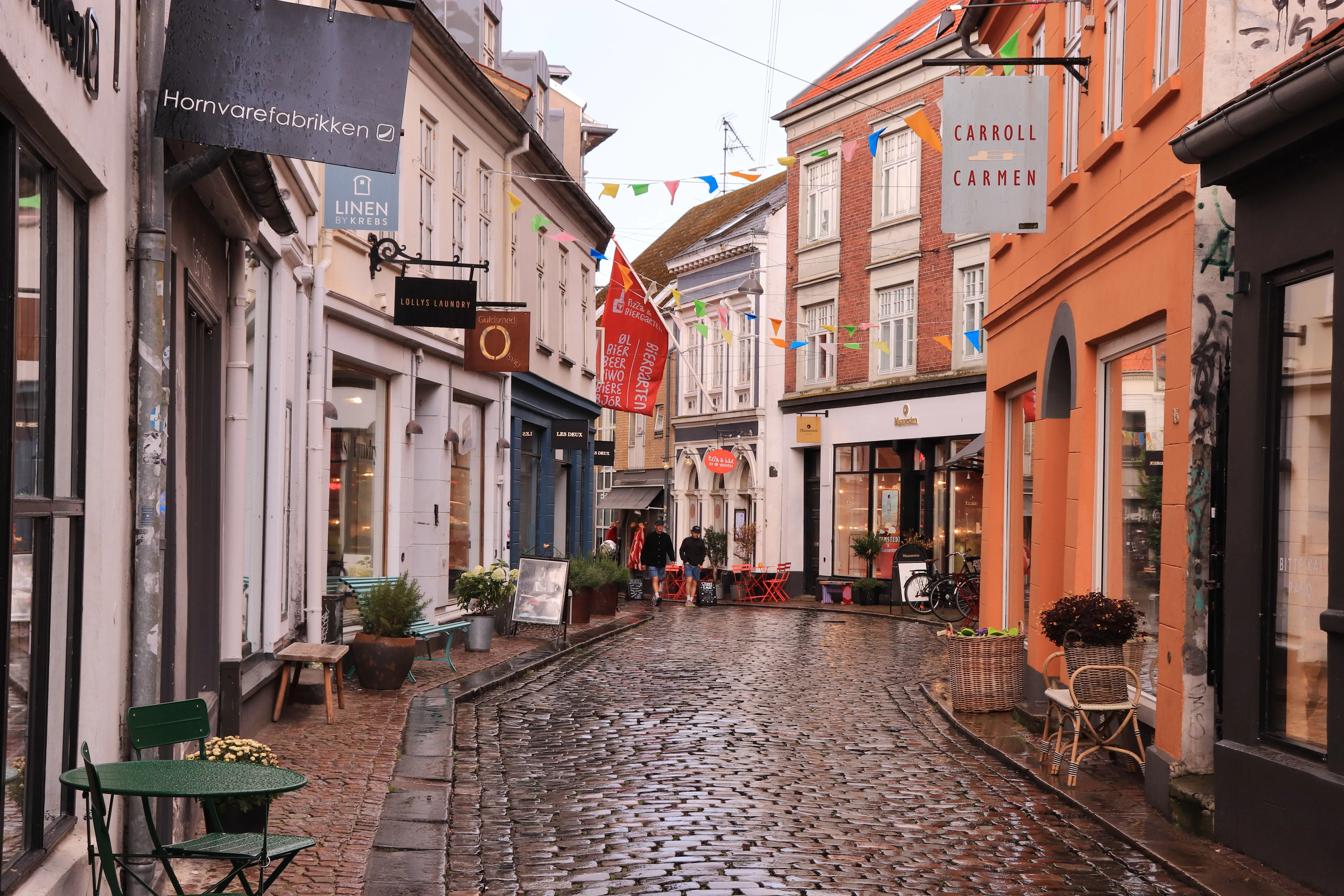 A street with cobblestones lined with two-story buildings and a sharp turn at the end.