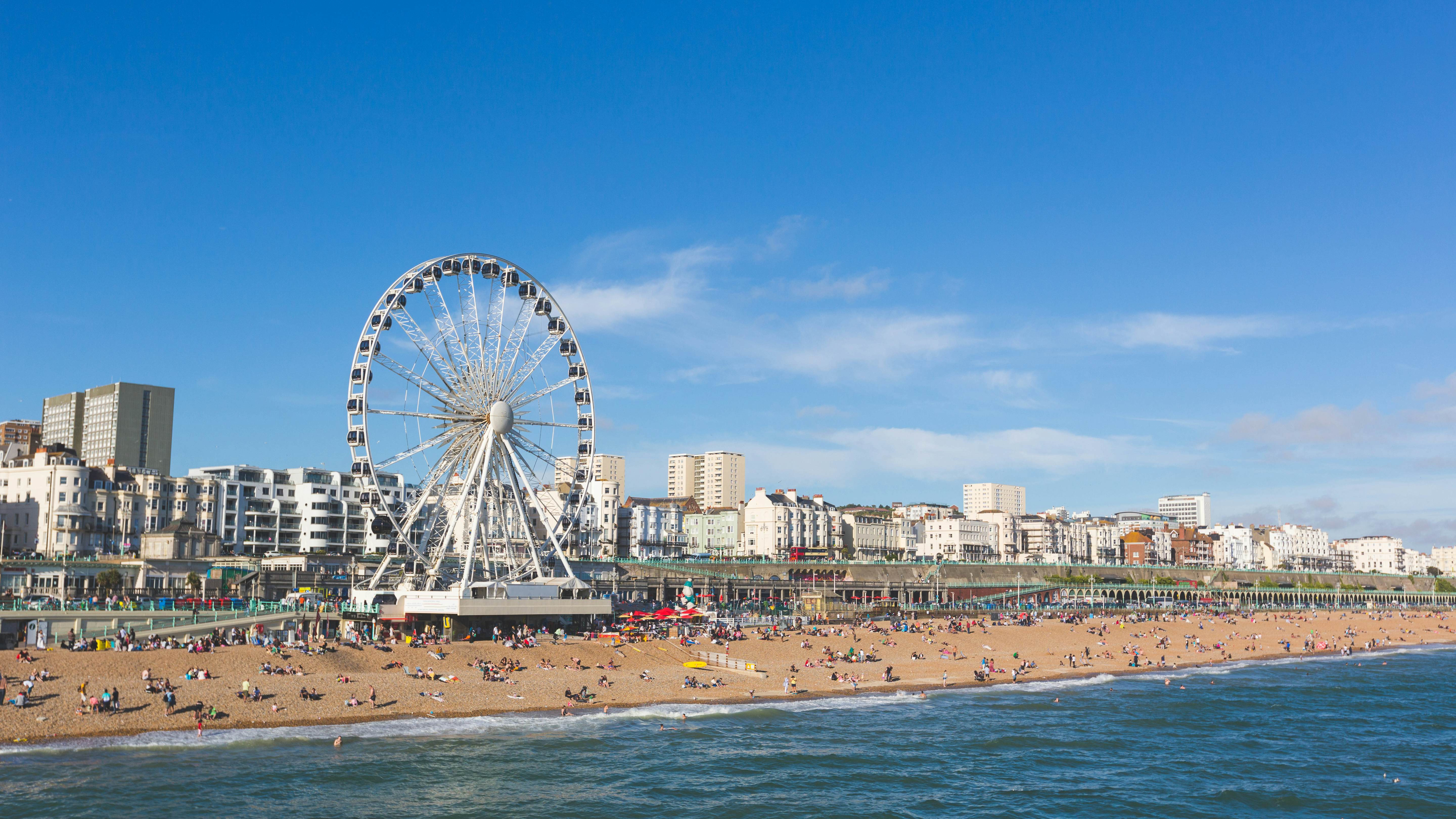 People gathered on a large pebbly beach overlooked by a Ferris wheel