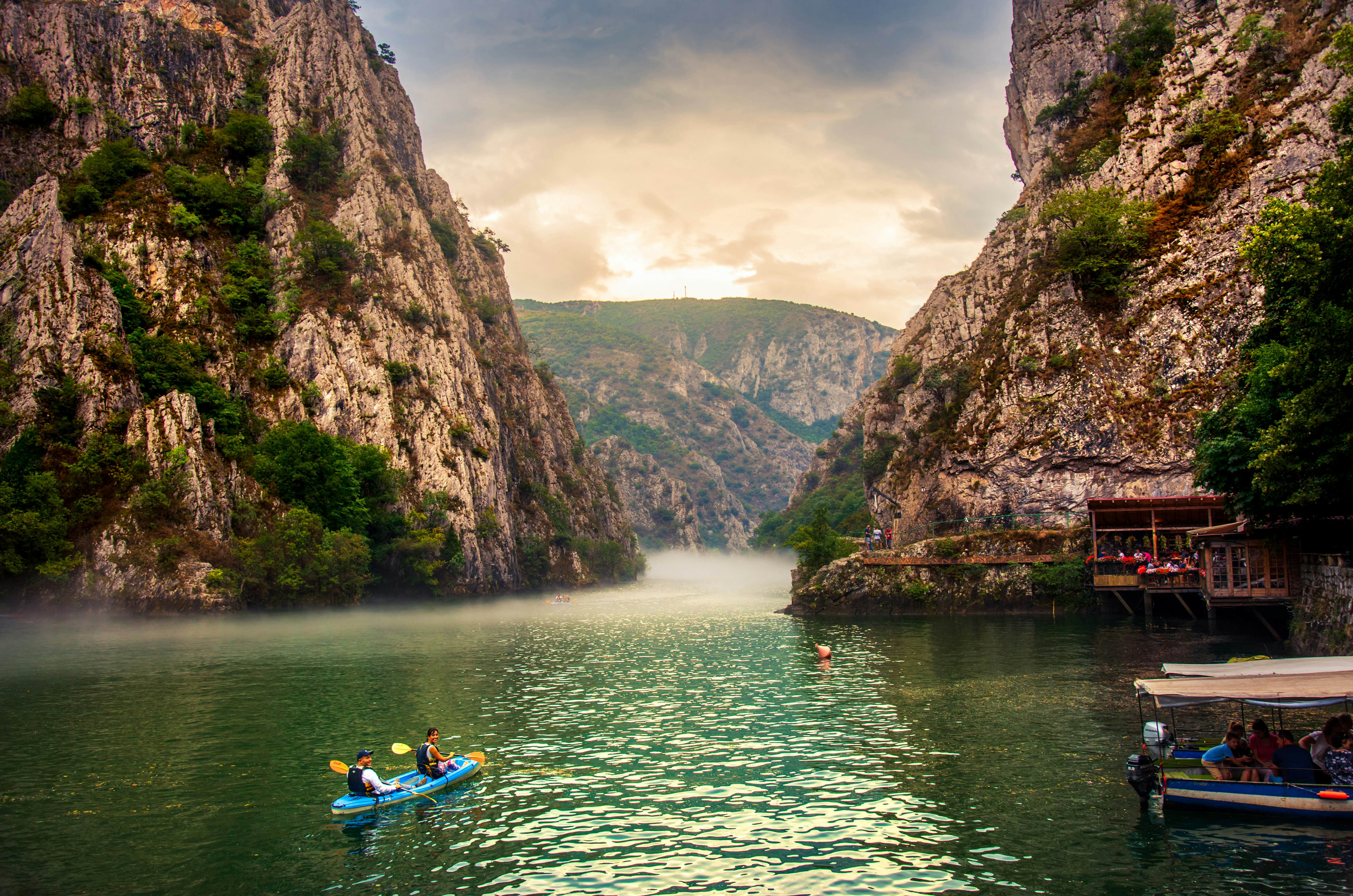 Kayakers paddle between the sheer rock sides of a canyon with mist on the water.