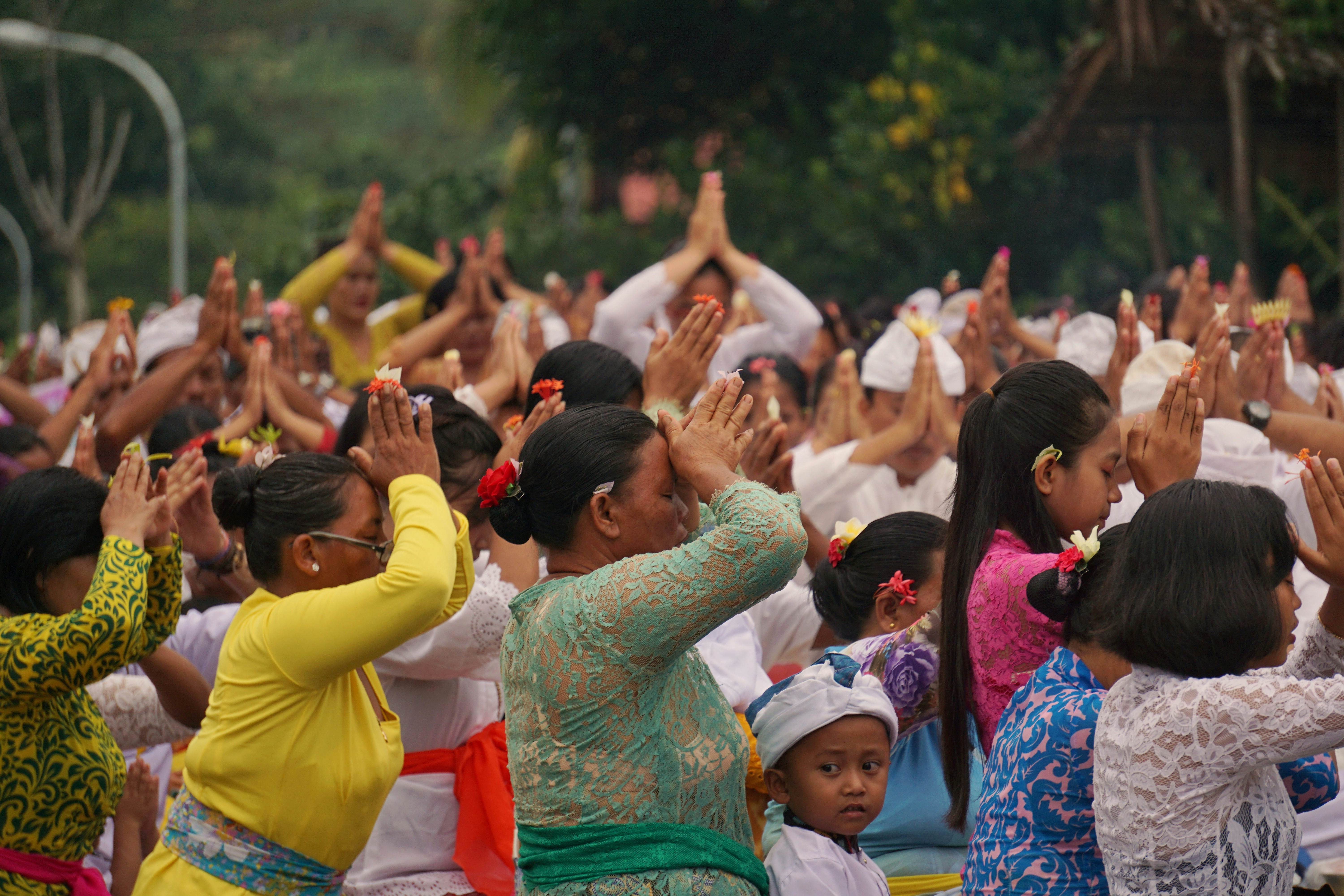 A crowd of women kneel and pray with their hands on their heads on a street.