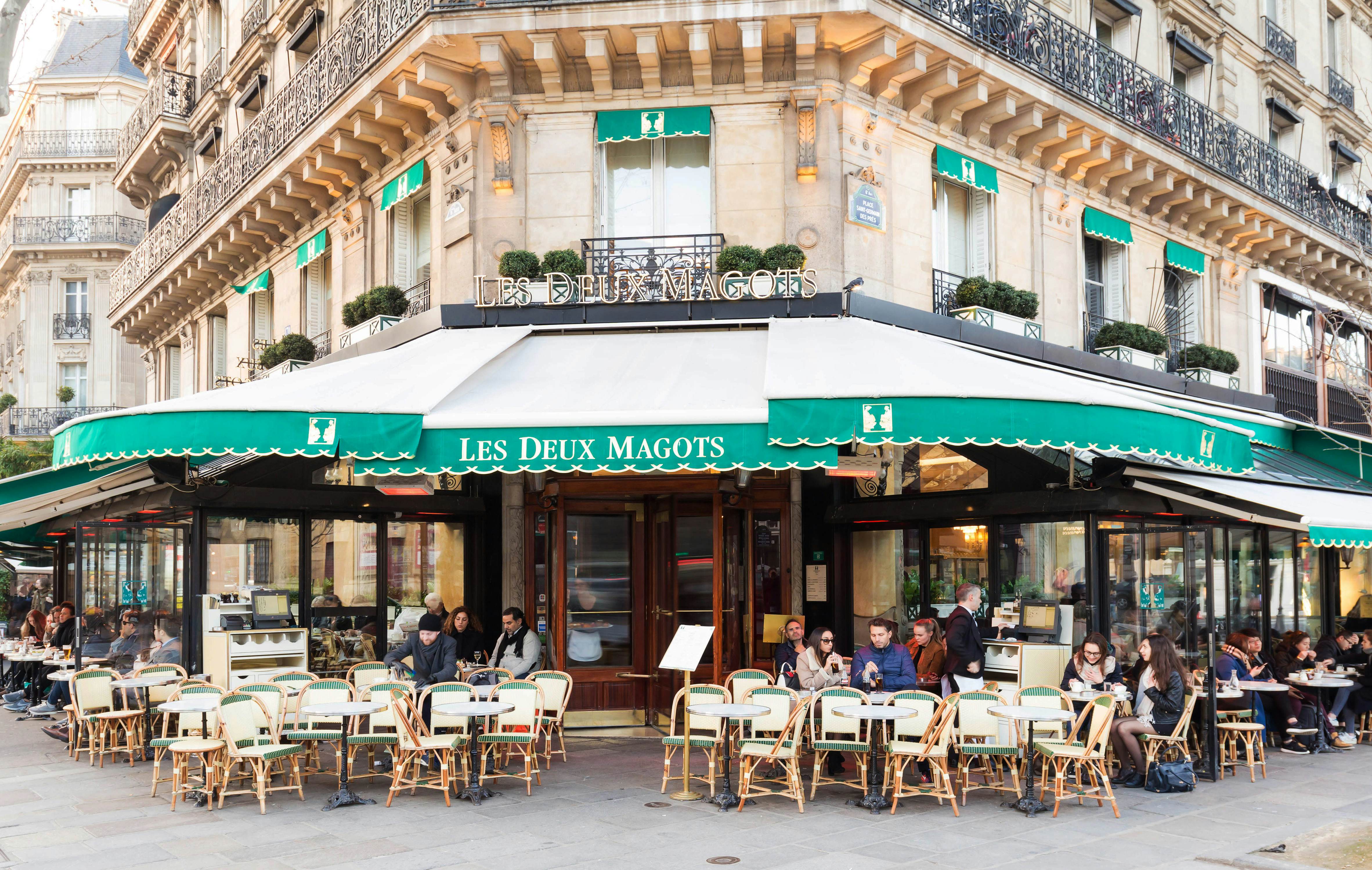 People gather at tables outside a traditional Parisian cafe