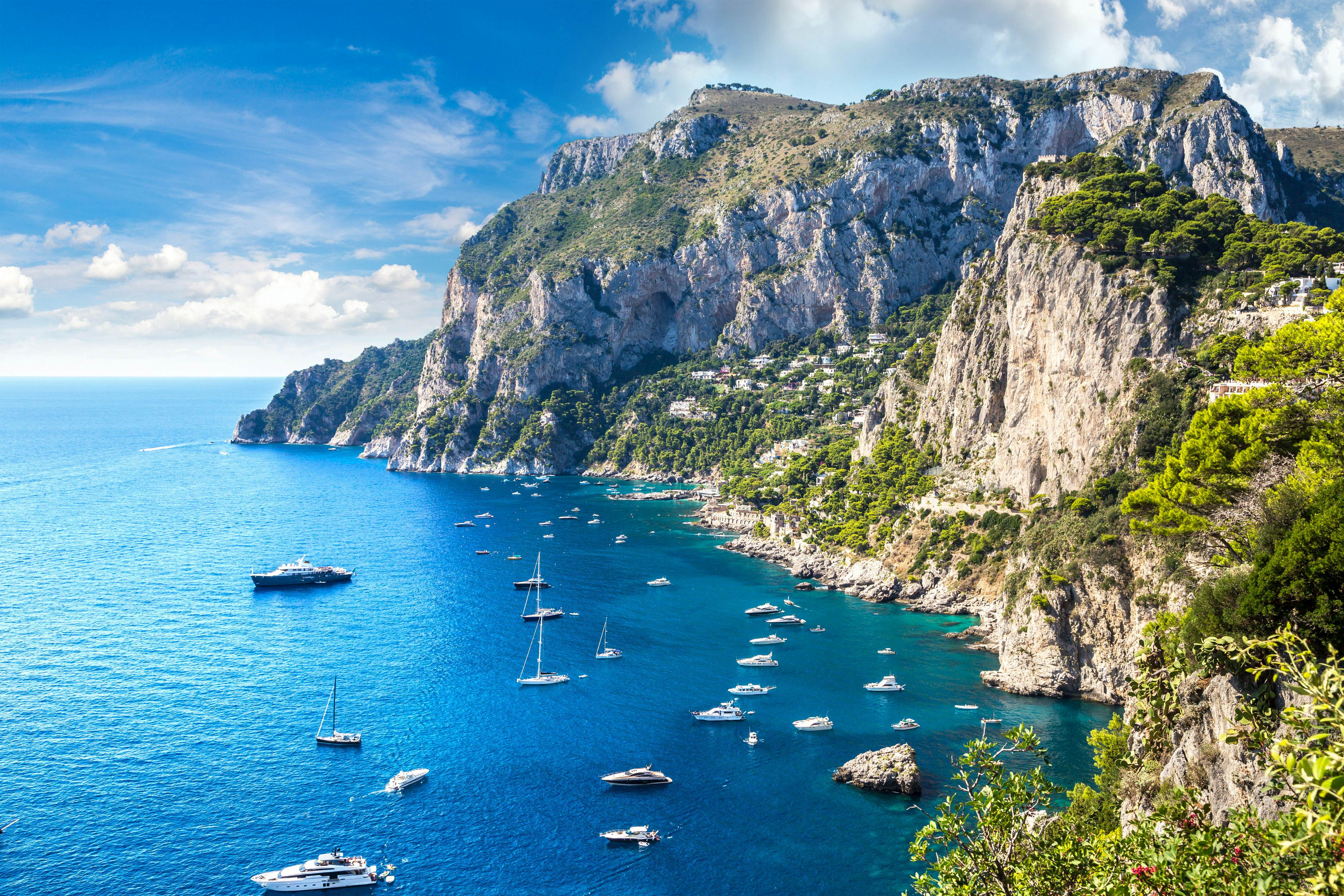 Boats anchored in a sheltered cove near a large rocky island on a sunny day