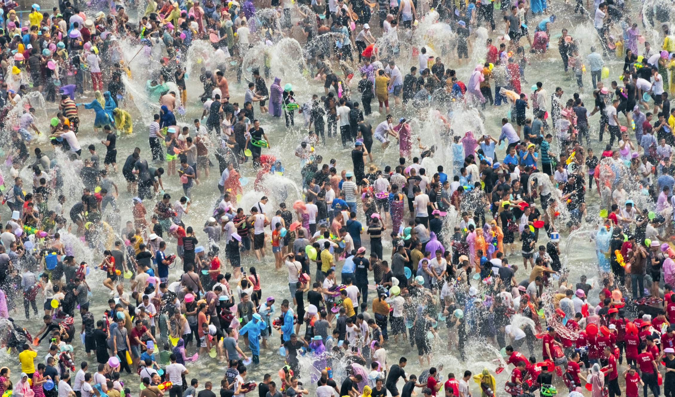 Huge crowds of people splashing in water and throwing buckets of water at each other in a colorful festival