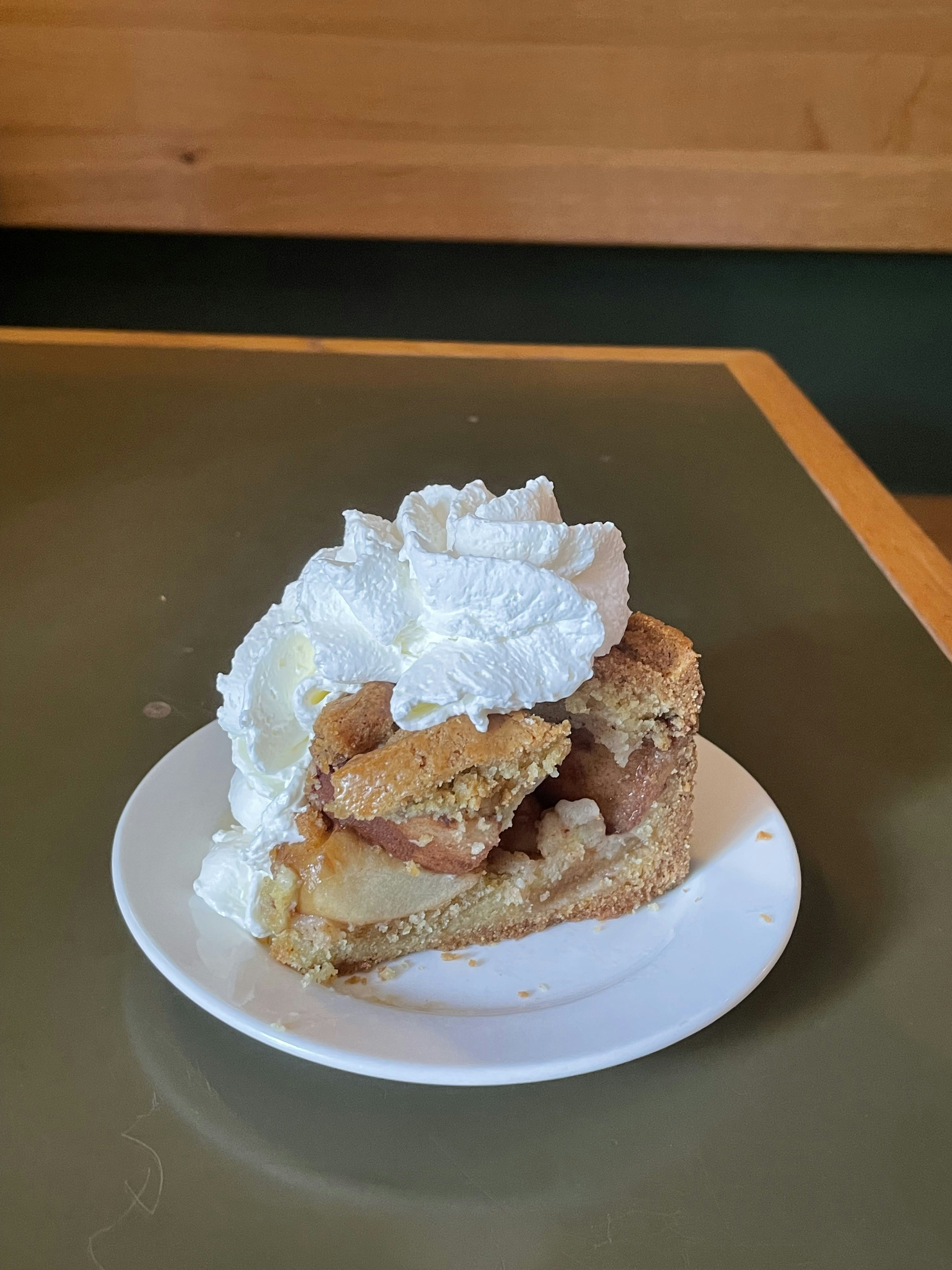 A white plate with a large piece of apple pie topped with thick whipped cream