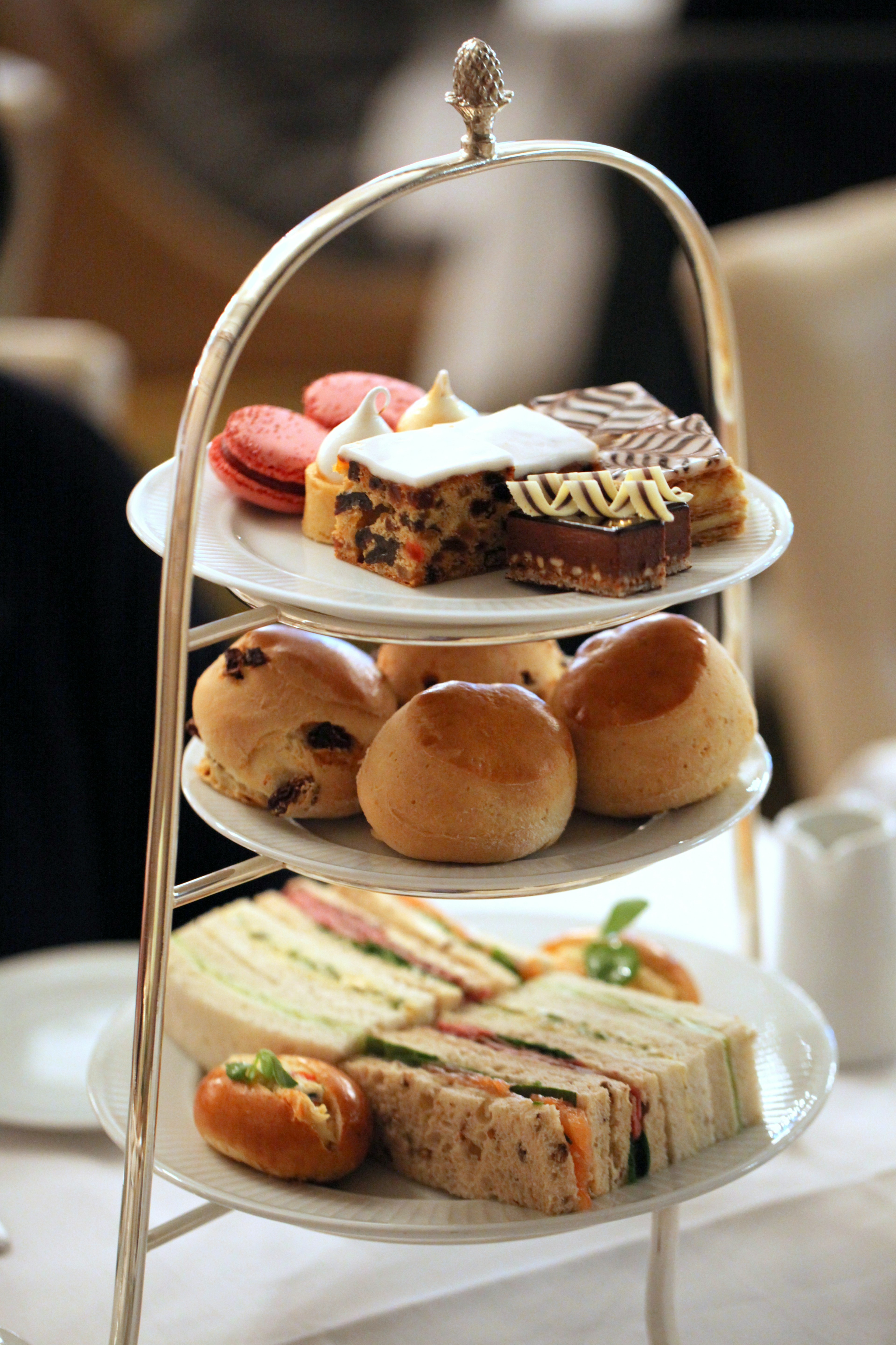 An assortment of sandwiches, cakes and pastries on a tiered display tray