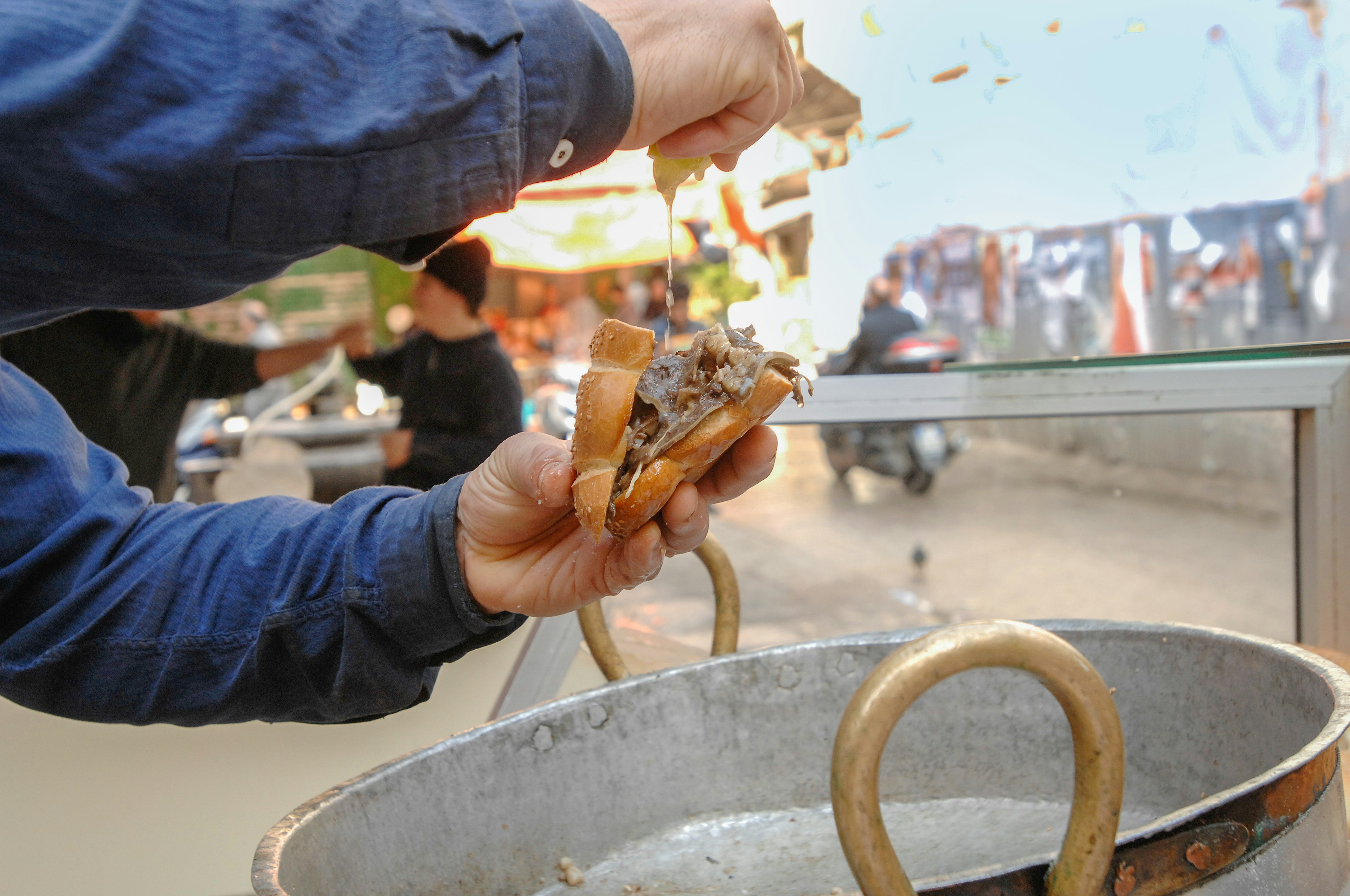 The arms of a person squeezing lemon over a sandwich with meat above a silver pan.