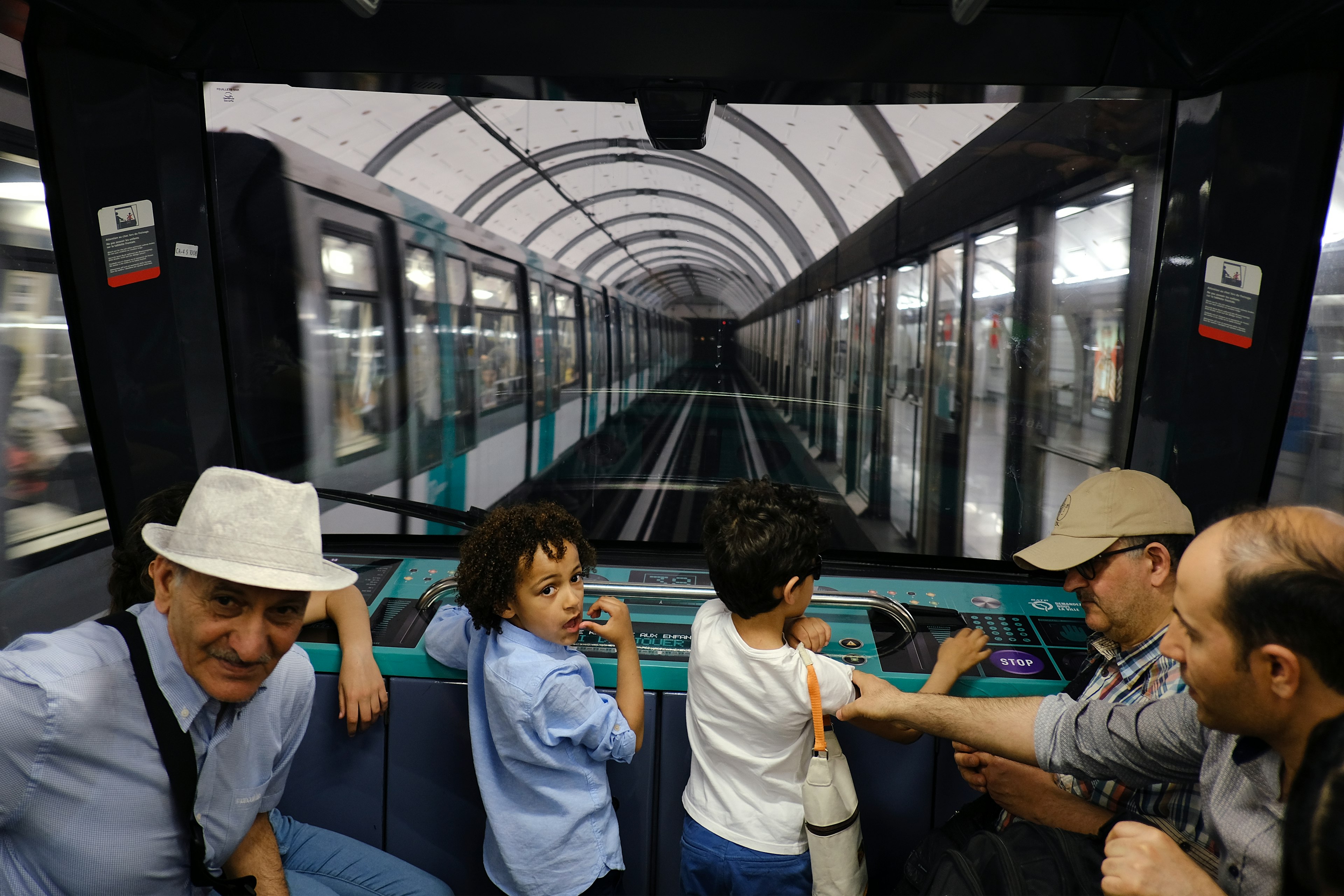 Children stand at the front of a subway car and watch the tracks through the windshield as the train pulls into a station.