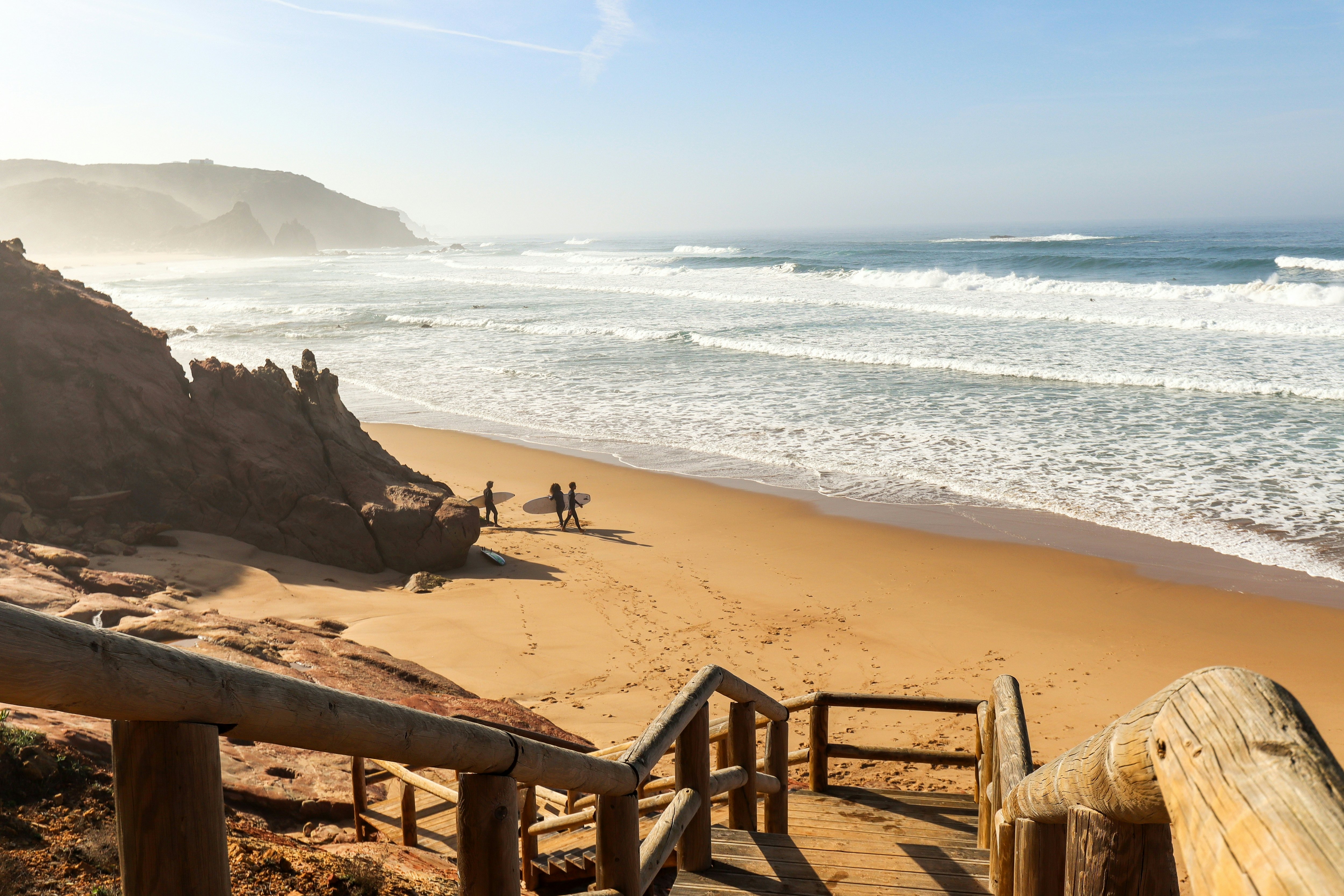 Three surfers on an empty sandy beach that's being pounded by Atlantic waves.