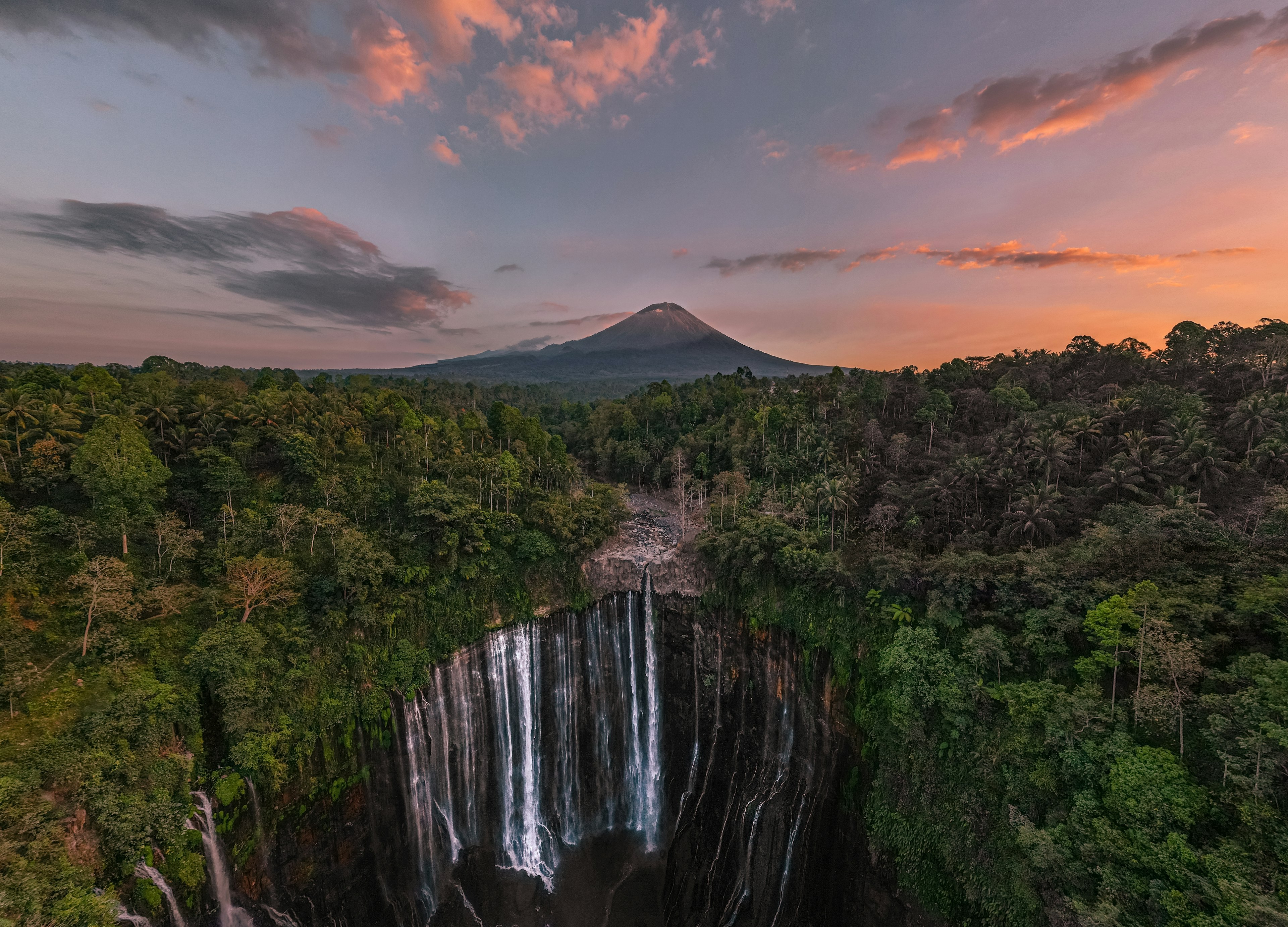 Aerial view of Tumpak Sewu waterfall at sunrise with Mount Semeru in the background, East Java, Indonesia.