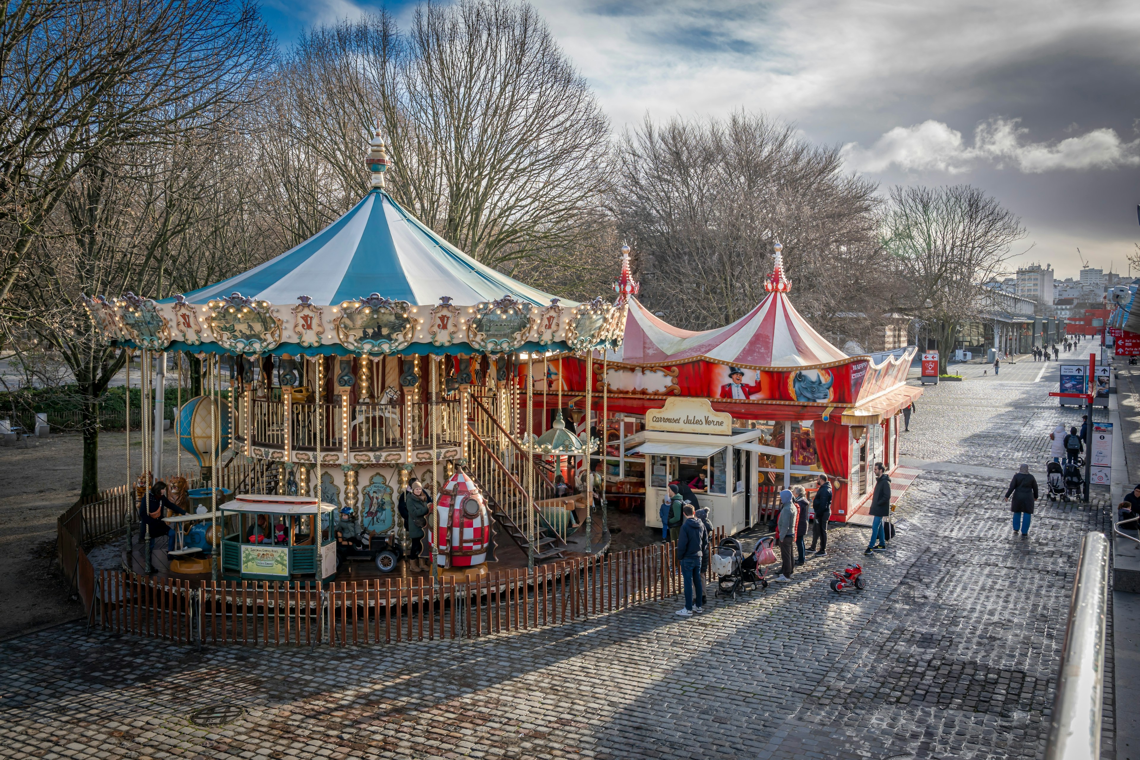 A view of a small carousel and other amusements in a city park on a winter afternoon.