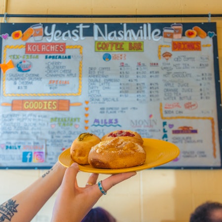 Kolaches at Yeast, held up in front of the menu written on the wall