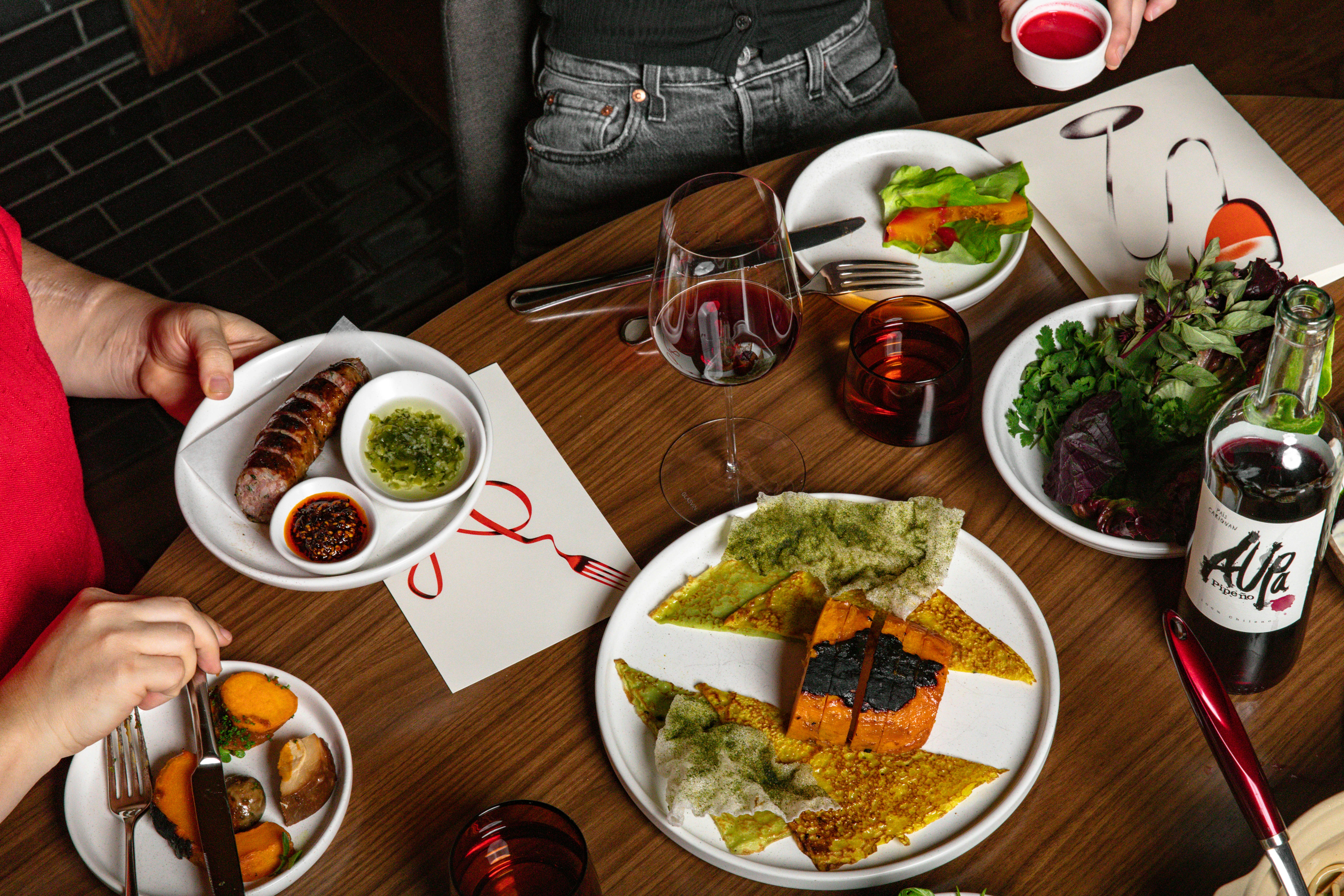 Plates of food spread out across a table with glasses of wine