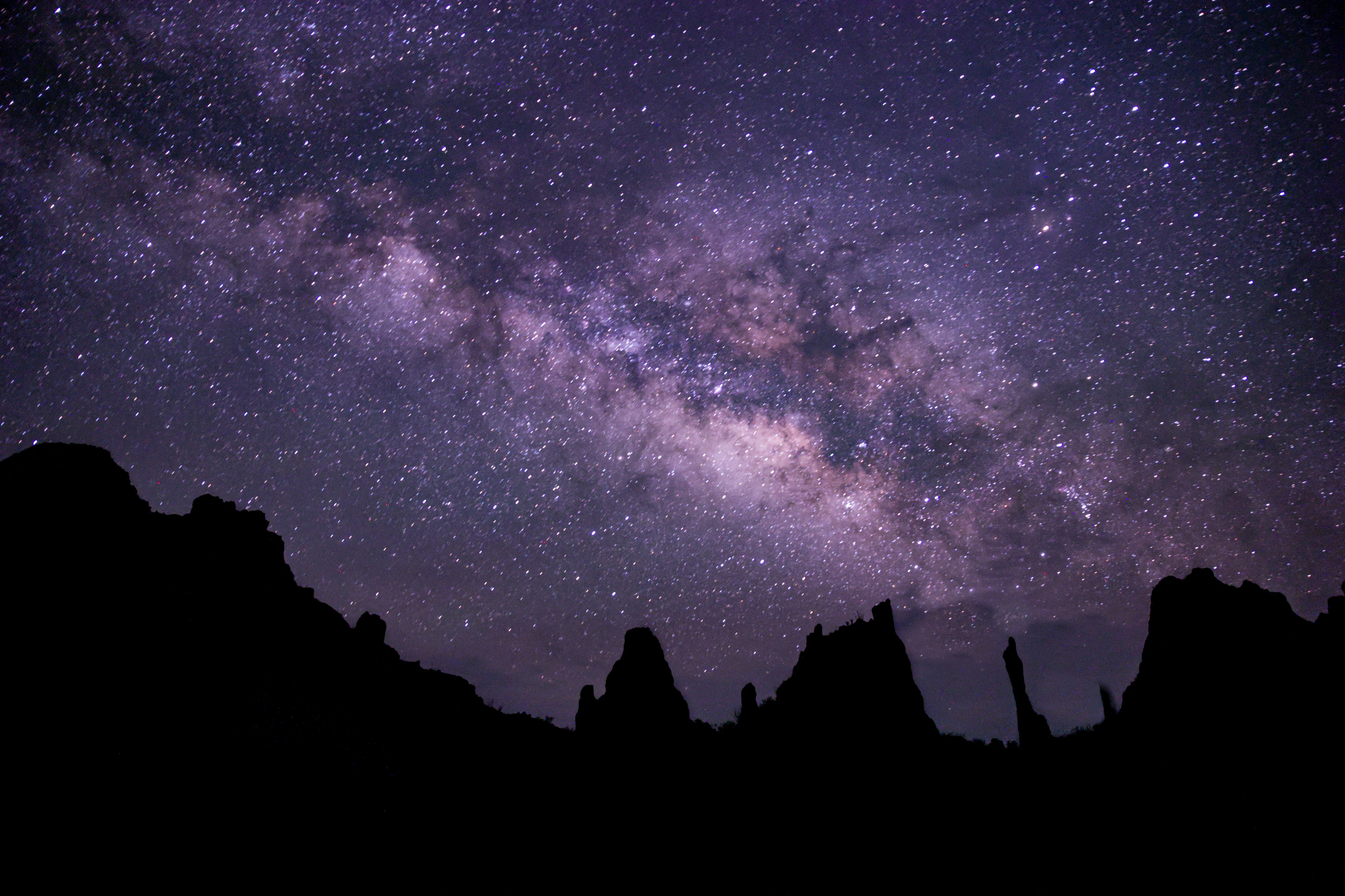 A night sky dense with stars and the Milky Way is seen over a silhouetted line of rocky crags.