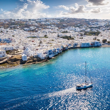 High-angle view of a sailing boat passing the village of Ornos.
1076454456
Sea, Yacht, Water, Photography, Mykonos, Cloud - Sky, Sky, Beauty In Nature, Building Exterior, Nature, Day, Aerial View, Color Image, Outdoors, High Angle View, Travel Destinations, Horizontal, Greece, Built Structure, Cityscape, Architecture, Town, Summer, Waterfront, City, Tourism, Travel, Sailboat, Island, No People, Turquoise Colored, Transportation, Nautical Vessel