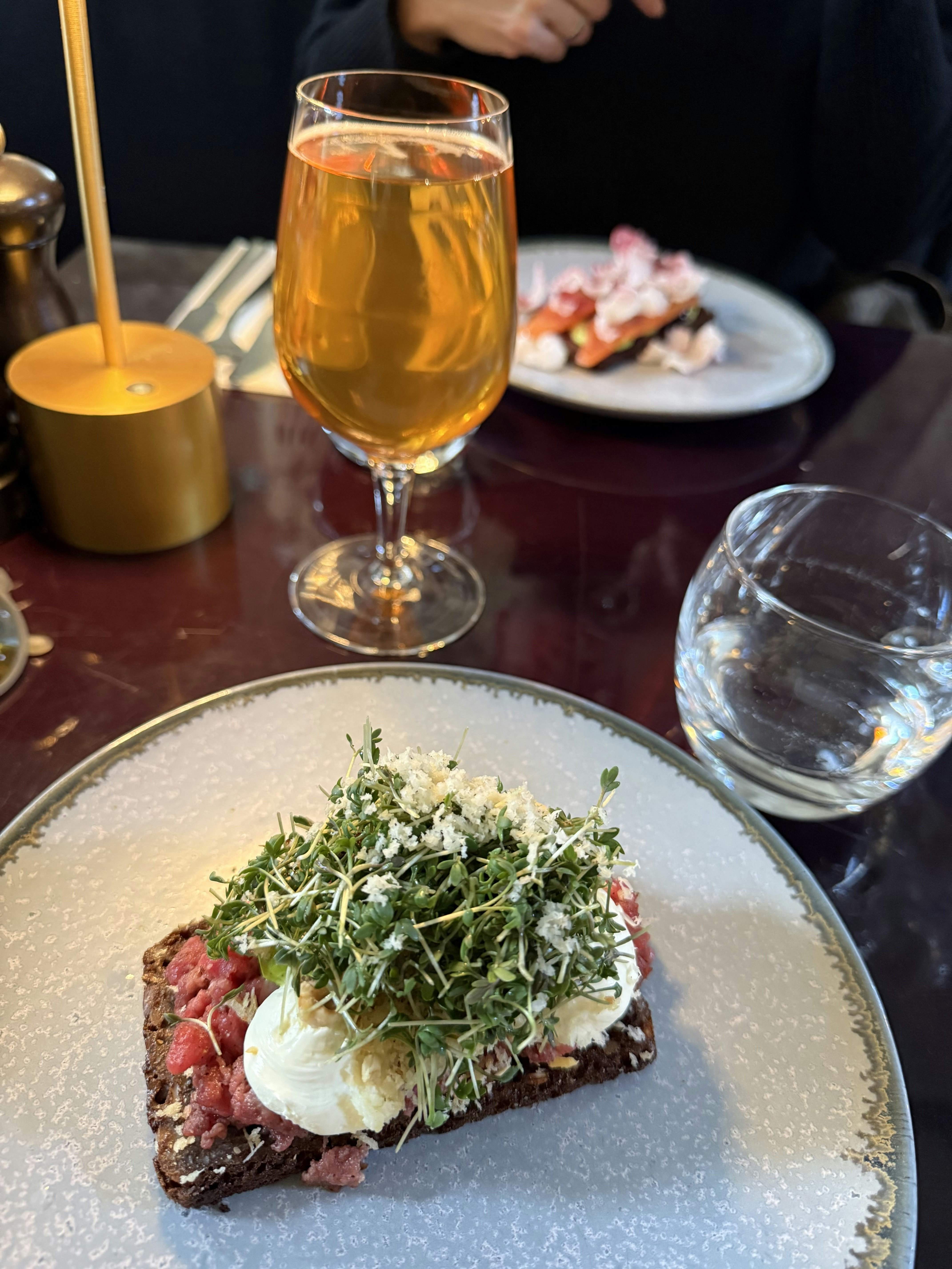 Close-up of beef tartare smørrebrød on a plate with glasses in the background.