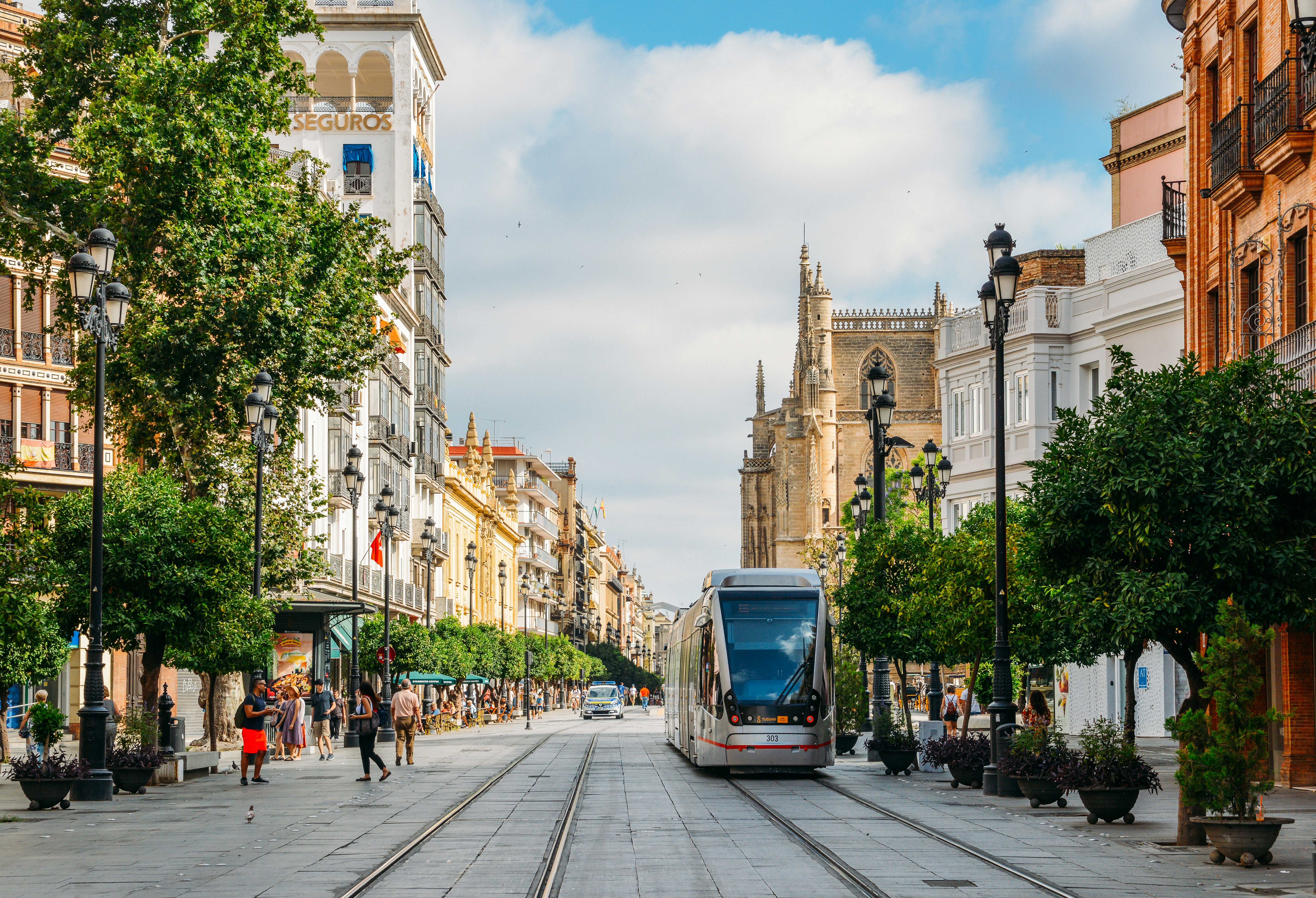 Electric tram on Constitution Avenue with iconic Seville Cathedral in background.