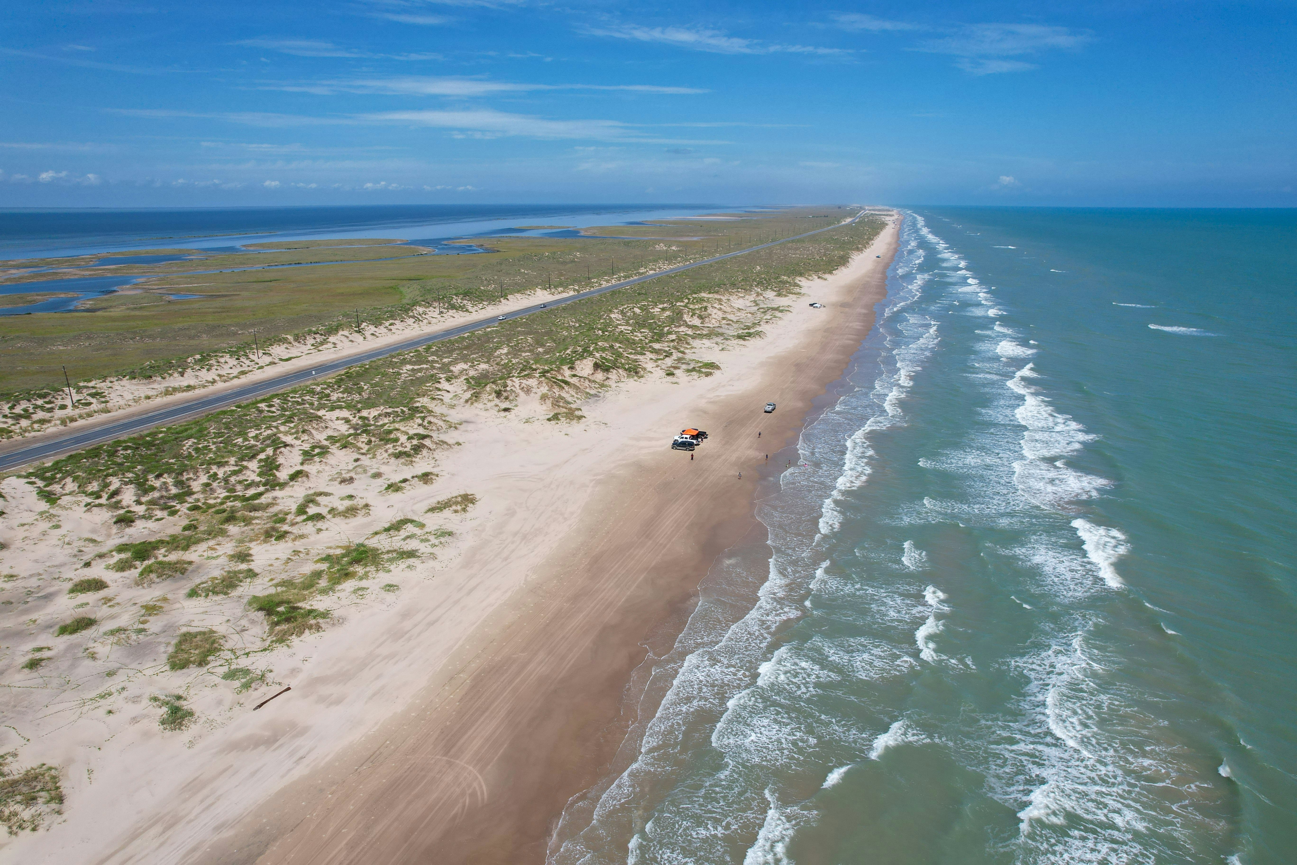 An aerial view of a near-deserted beach on a long barrier island by the sea.