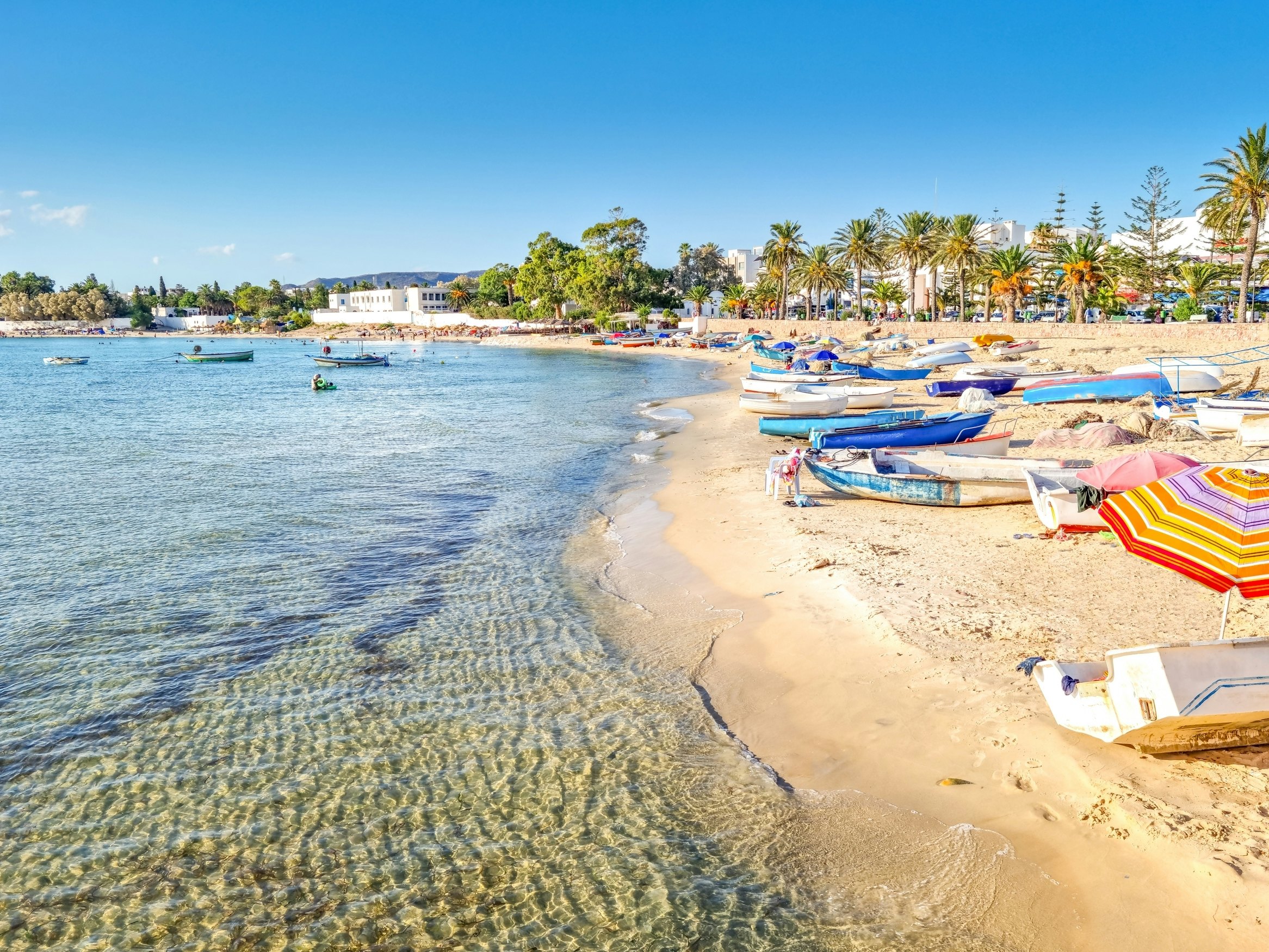 View of the beach in Hammamet, Tunisia, with boats and palm trees.