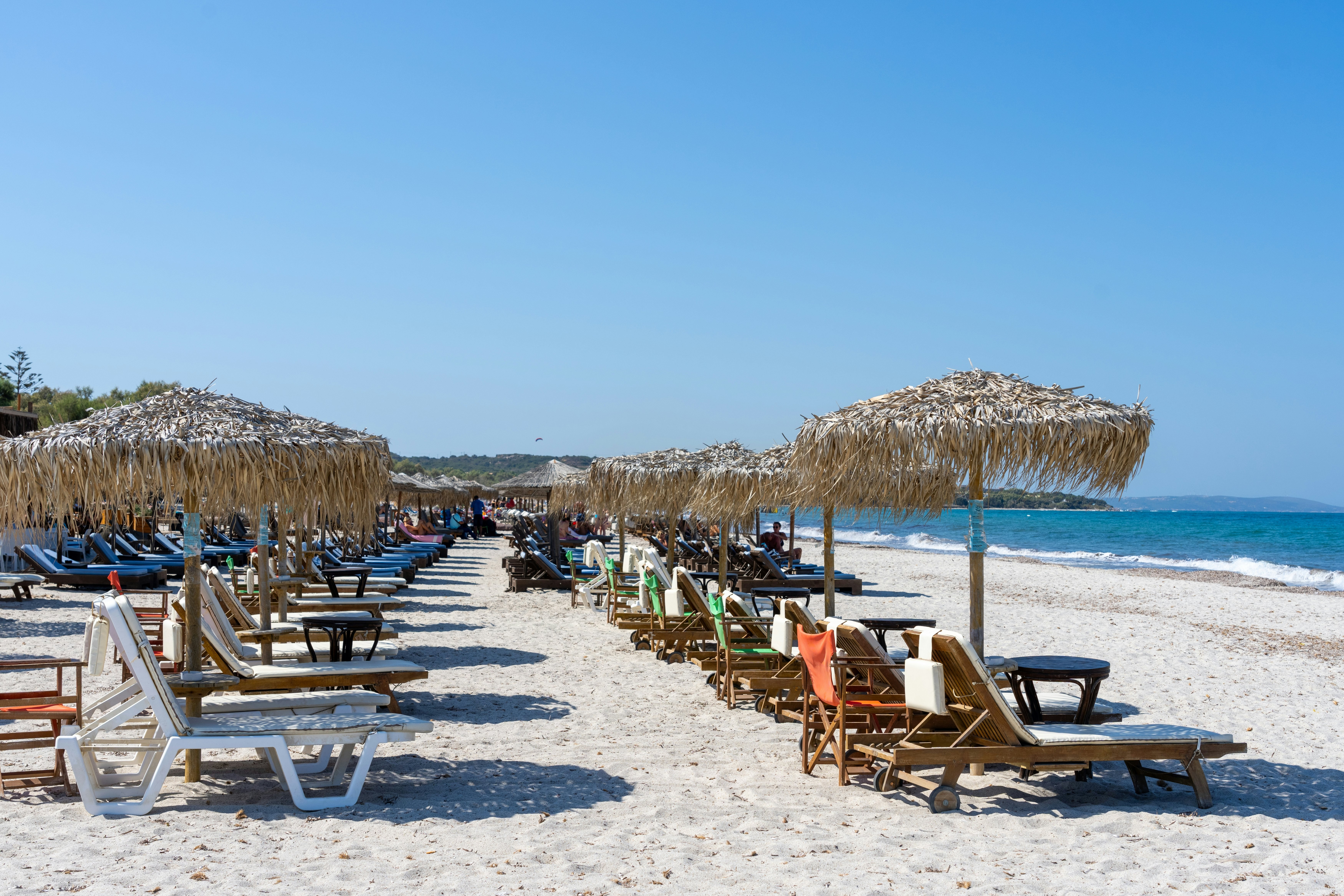 Sun loungers are lined up on a beach under straw umbrellas.