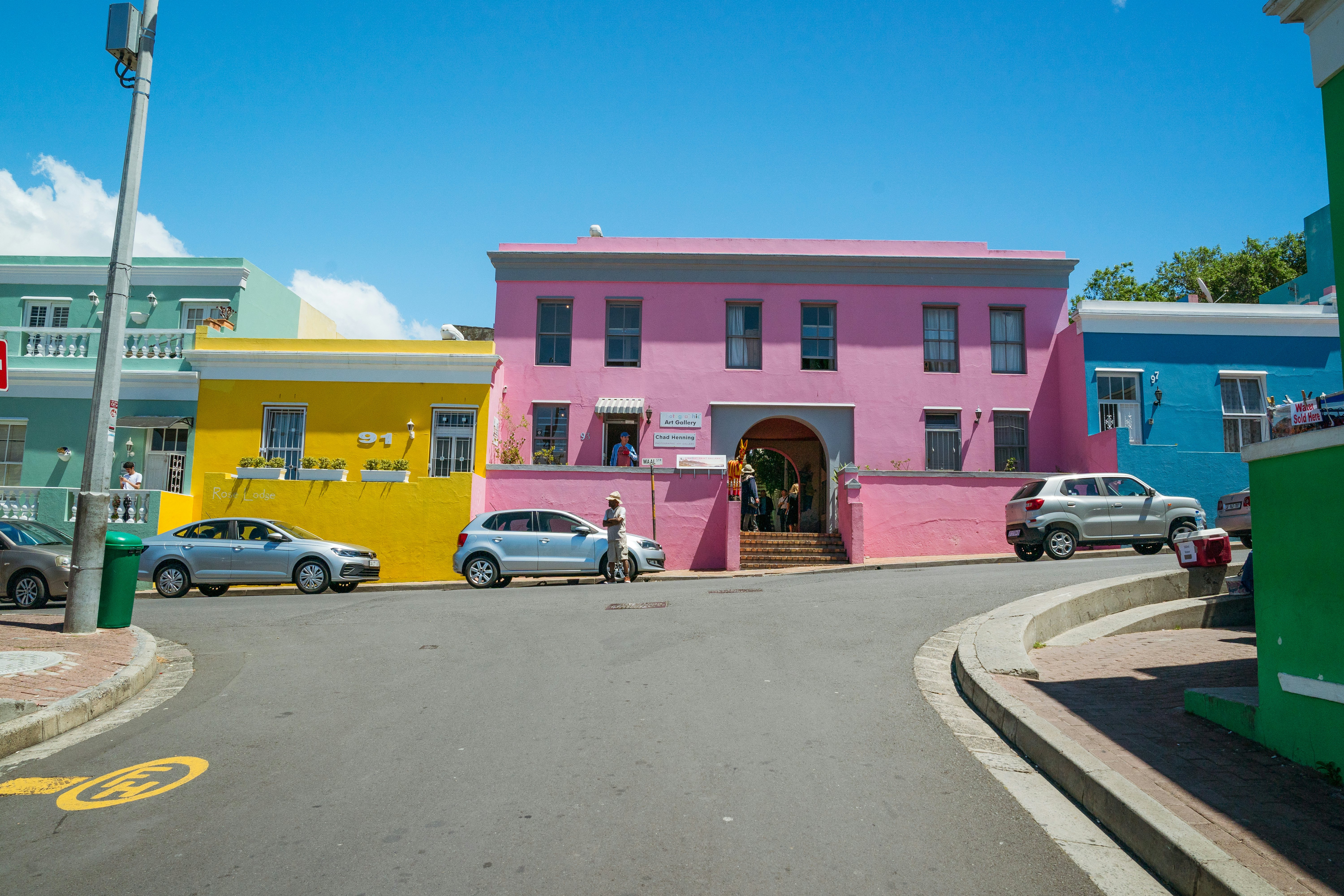 Pink, yellow, green, and blue houses along a roadway on a sunny day.