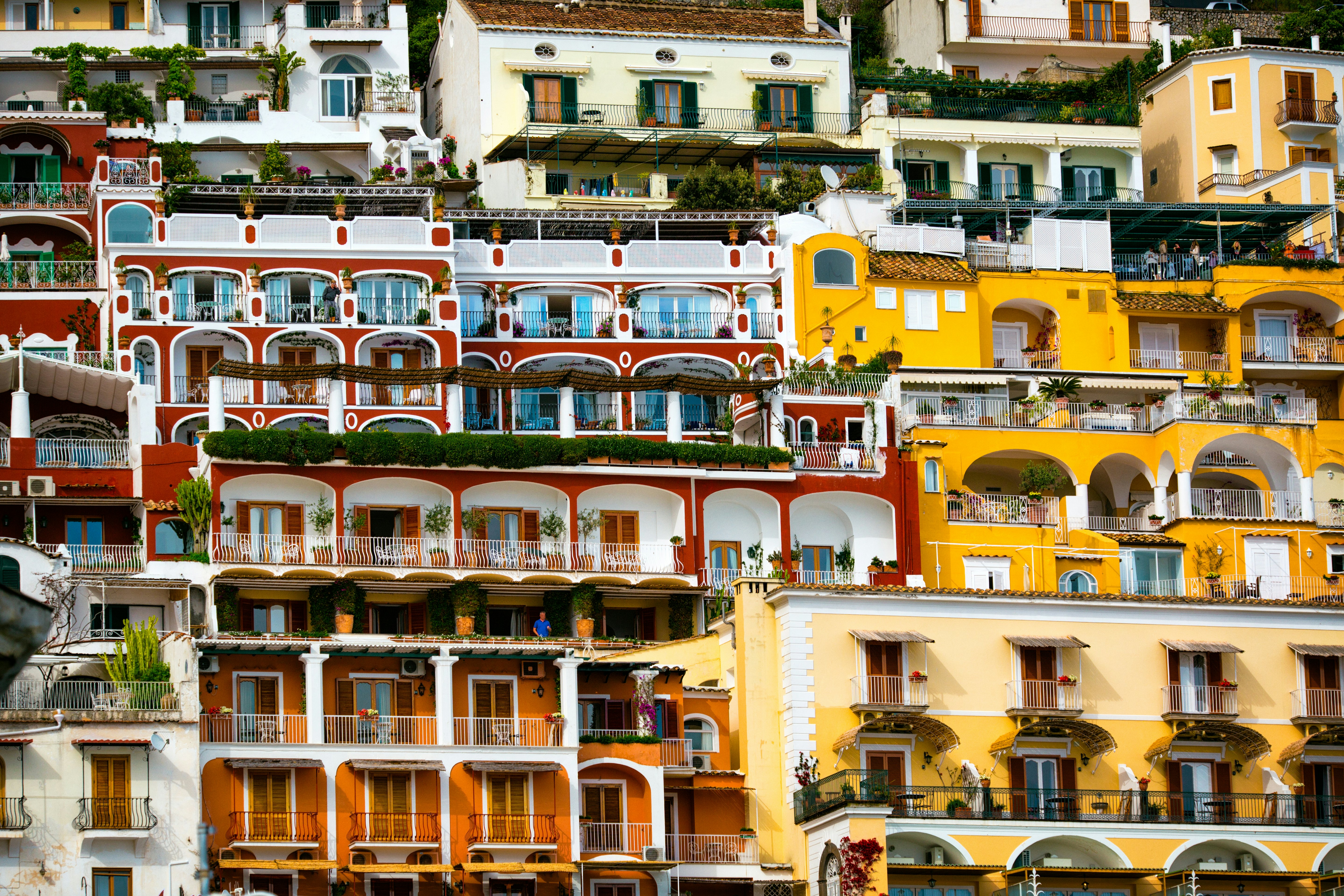Colorful buildings that appear stacked on top of one another in the side of a hill with many balconies and large shaded terraces.