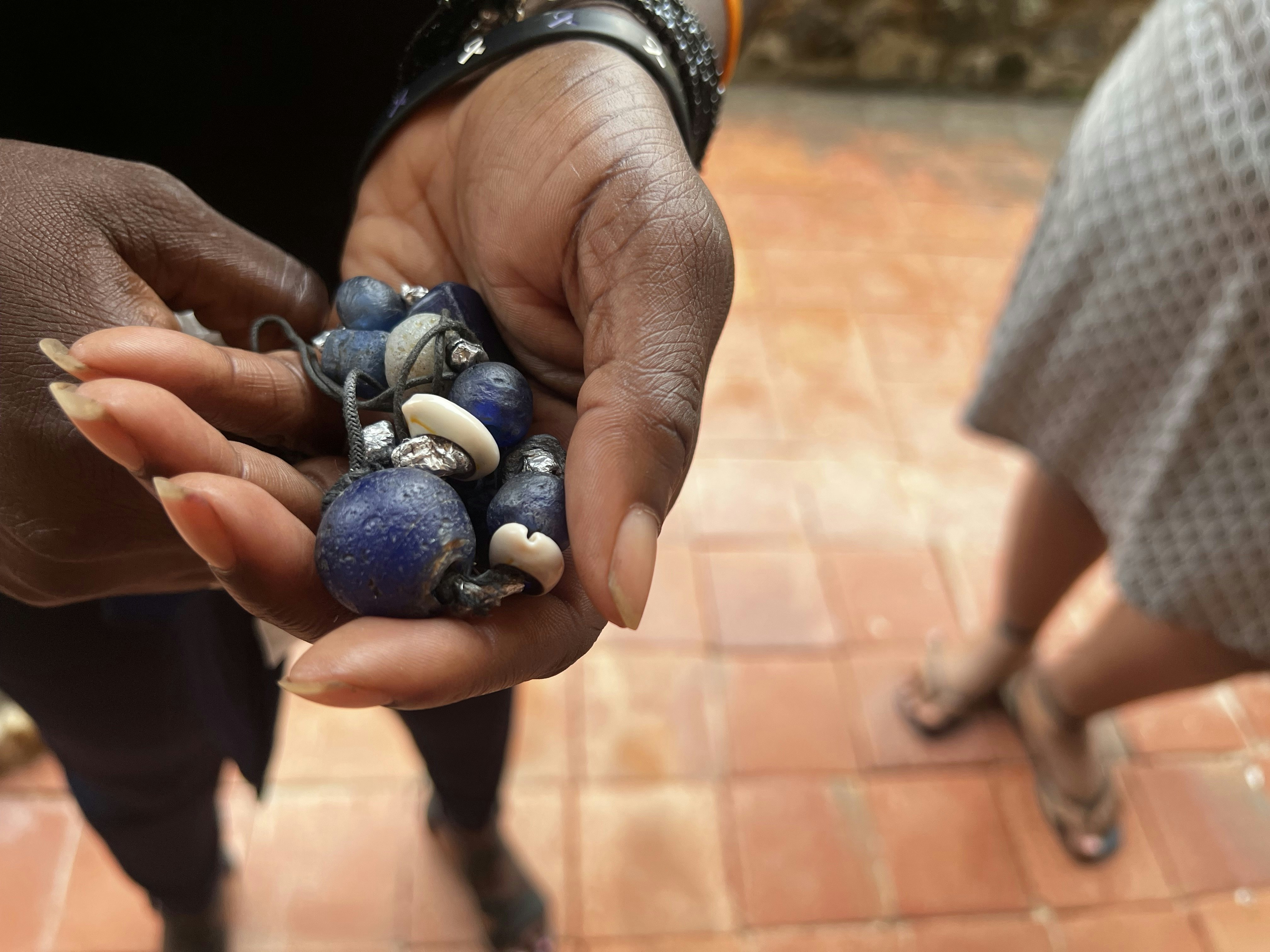 A hand holds a necklace with large round blue beads and smaller white shells.