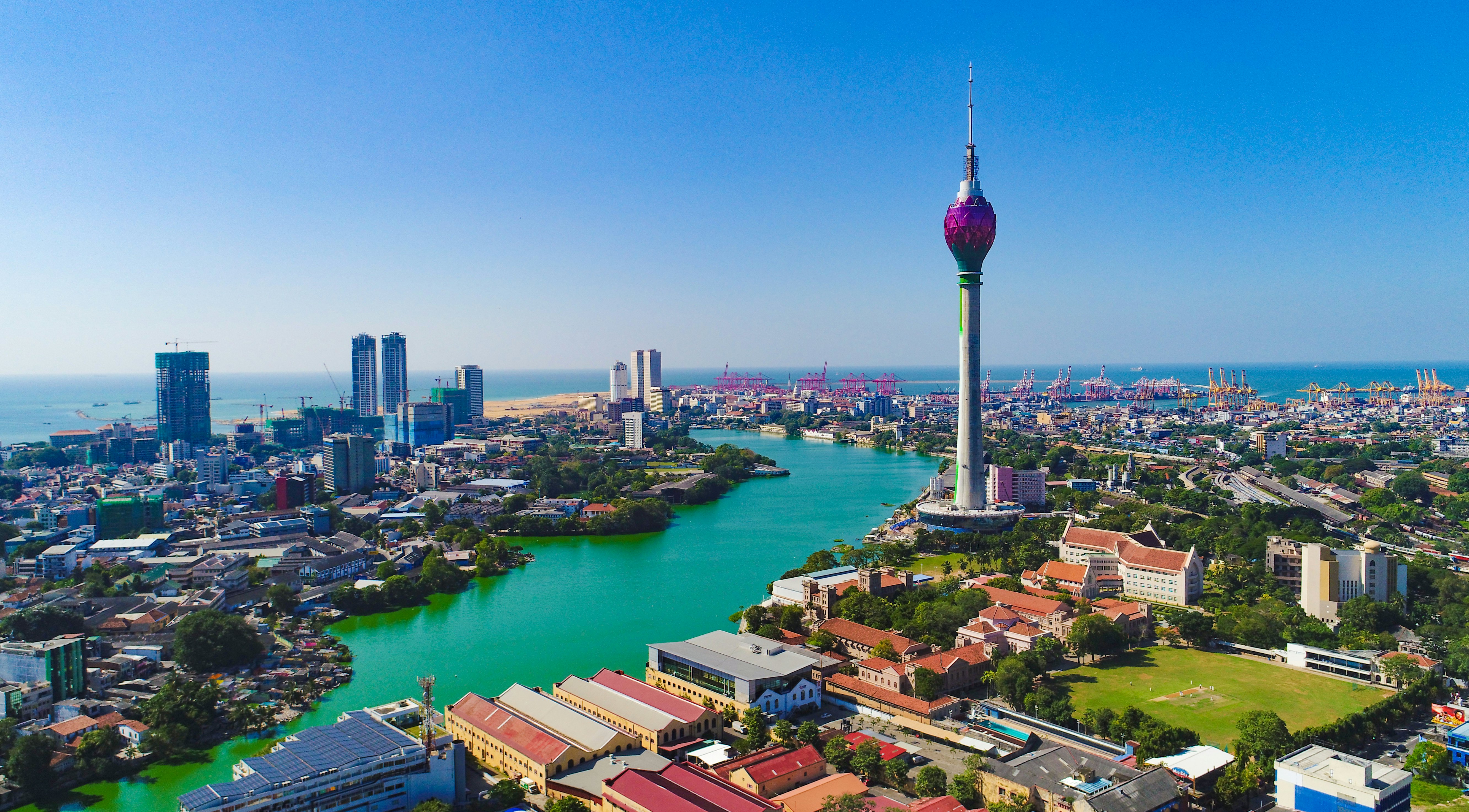 A cityscape with a tall modern TV tower and a river flowing to the sea.