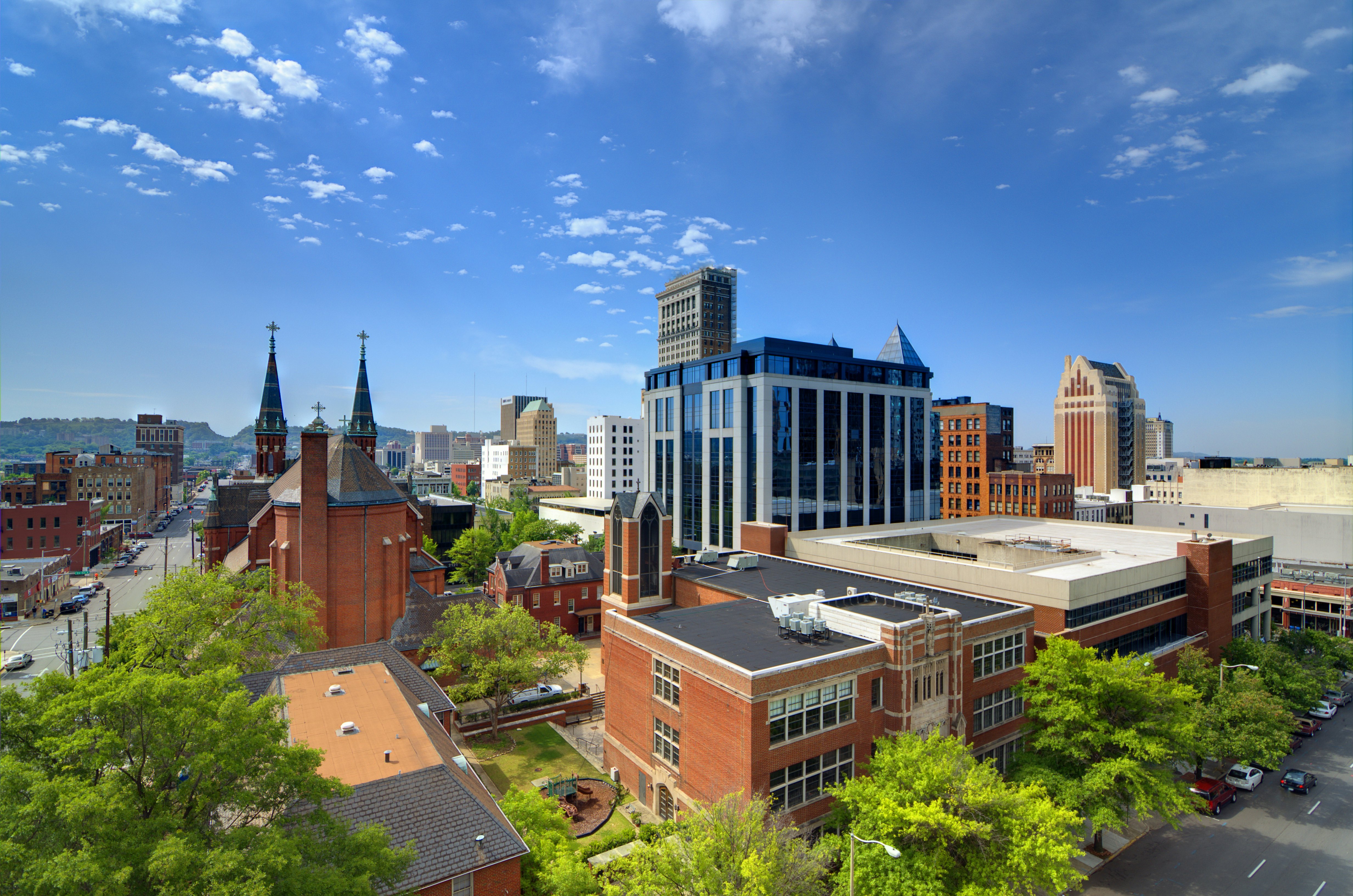 Red brick and modern glass city buildings under a blue, sunny sky.