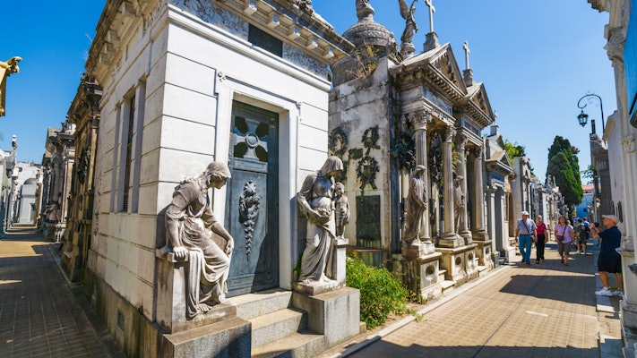 People walk on a path between elaborate carved mausoleums in Buenos Aires.
