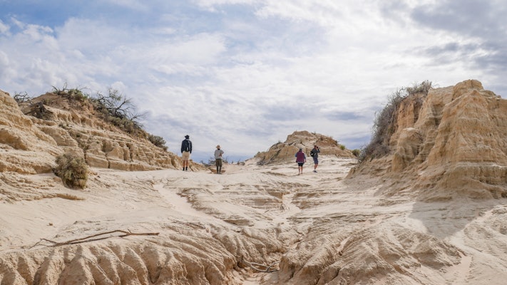 Four people walk through interesting rock formations in a desert scene