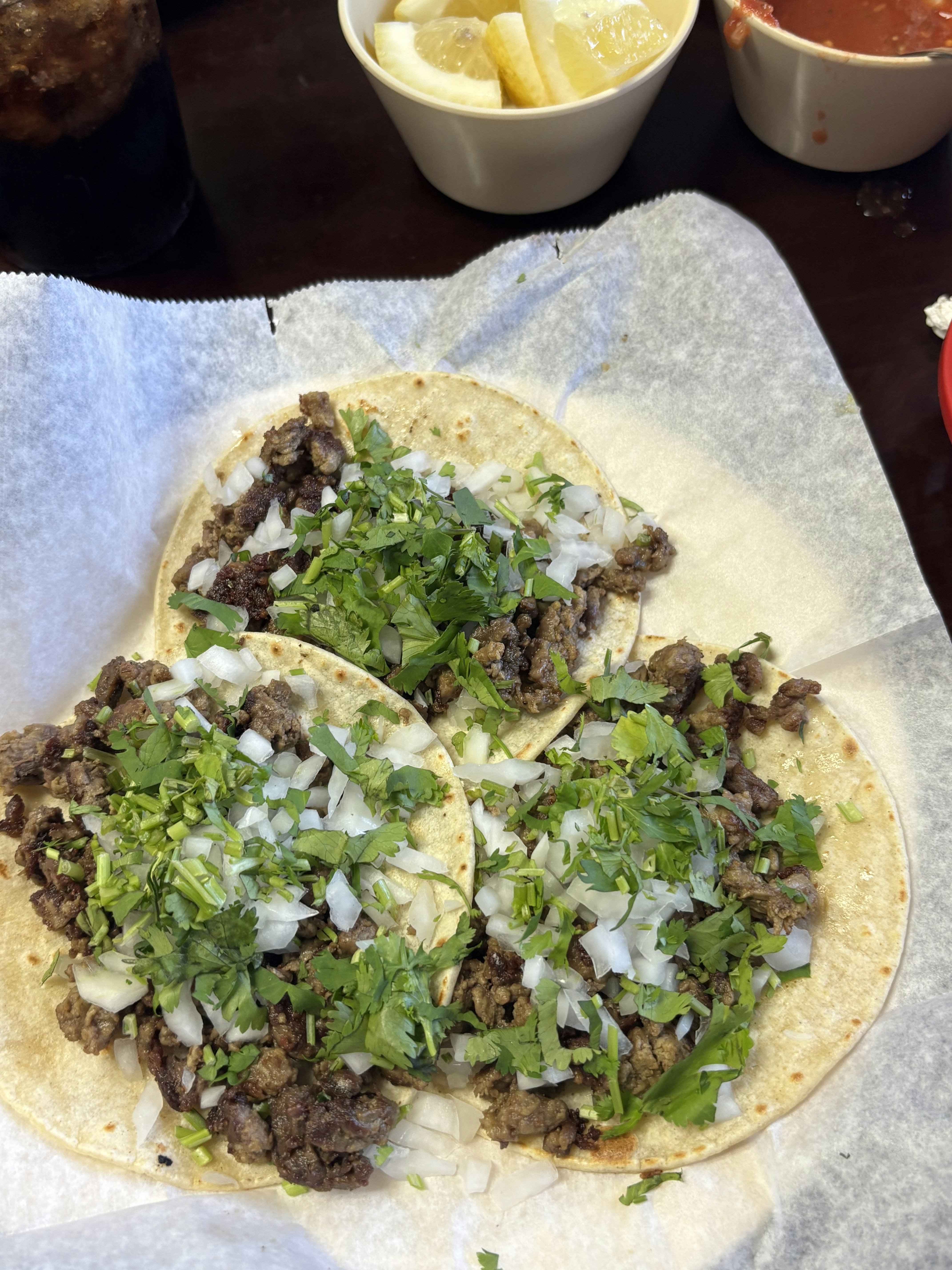 Three open soft taco shells topped with roasted beef, cilantro and onions