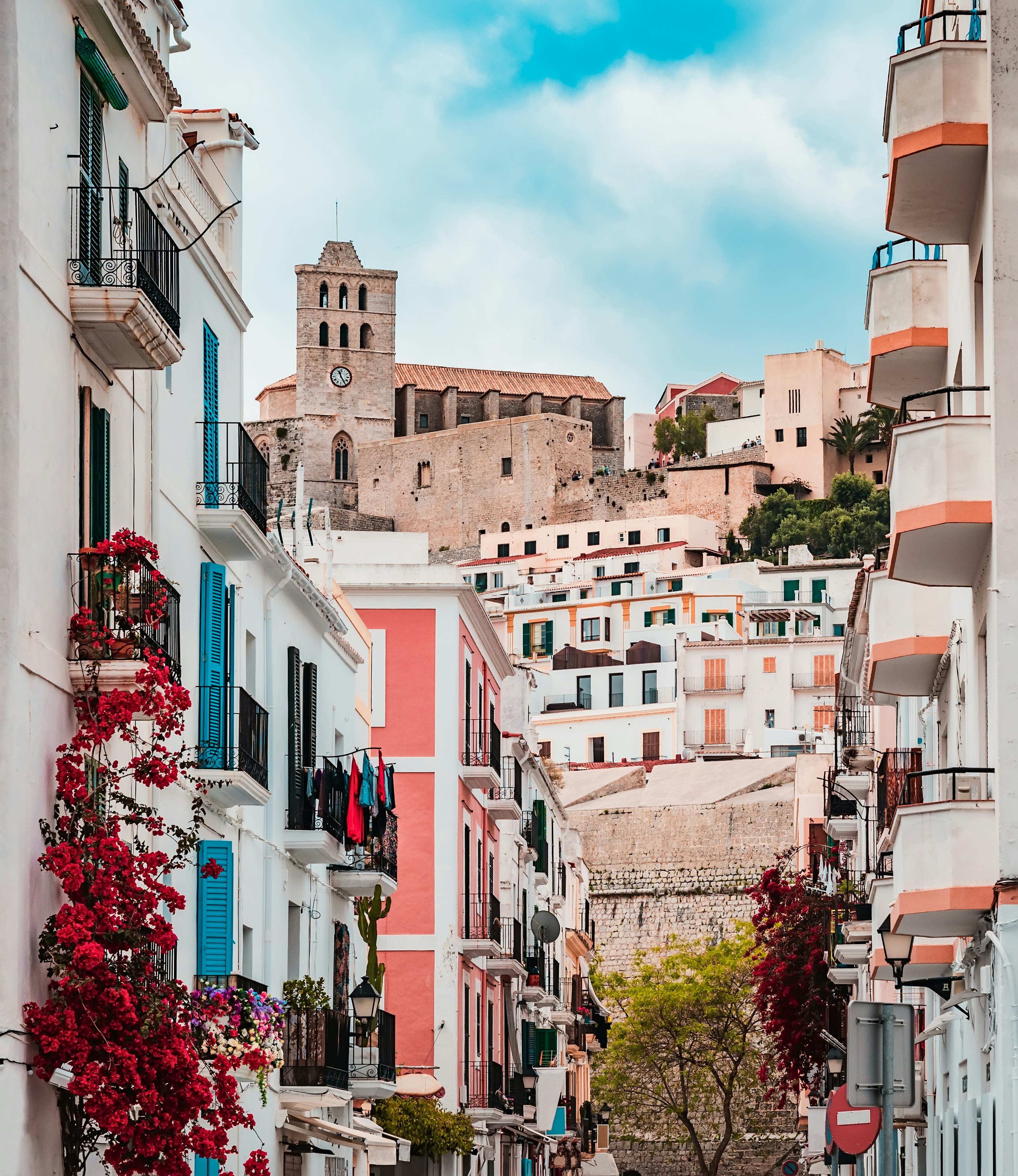 Bougainvillea on the facades of white buildings in an old Spanish town with a view of bastions and a church above