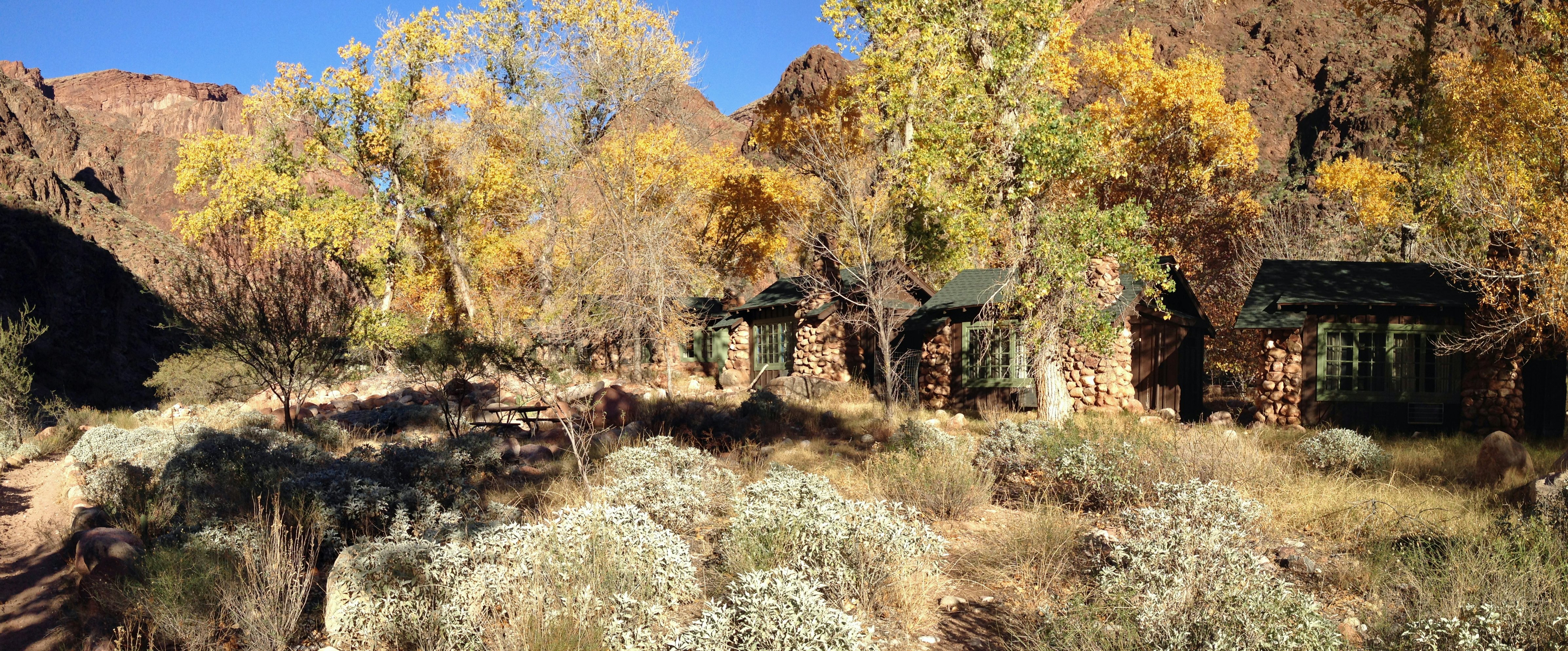 Stone cabins nestled among trees with red rock mountains in the background.
