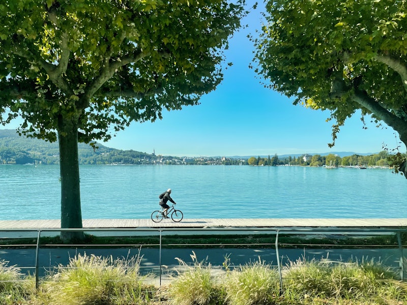 a cyclist is riding on his bicycle on a board walk a long the lake of annecy