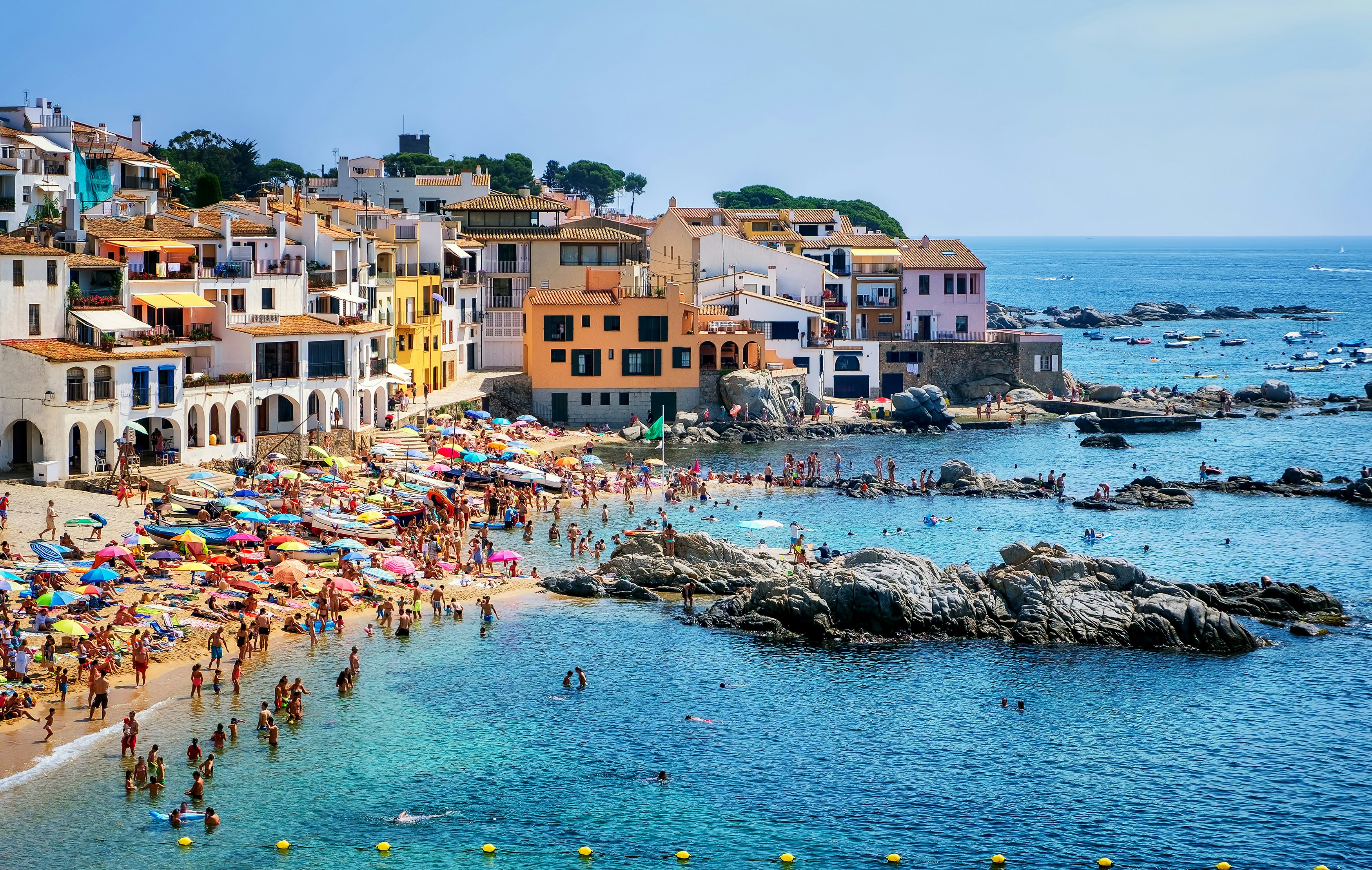 A busy cove on a summer's day with people in the water and under tightly-packed colorful parasols.