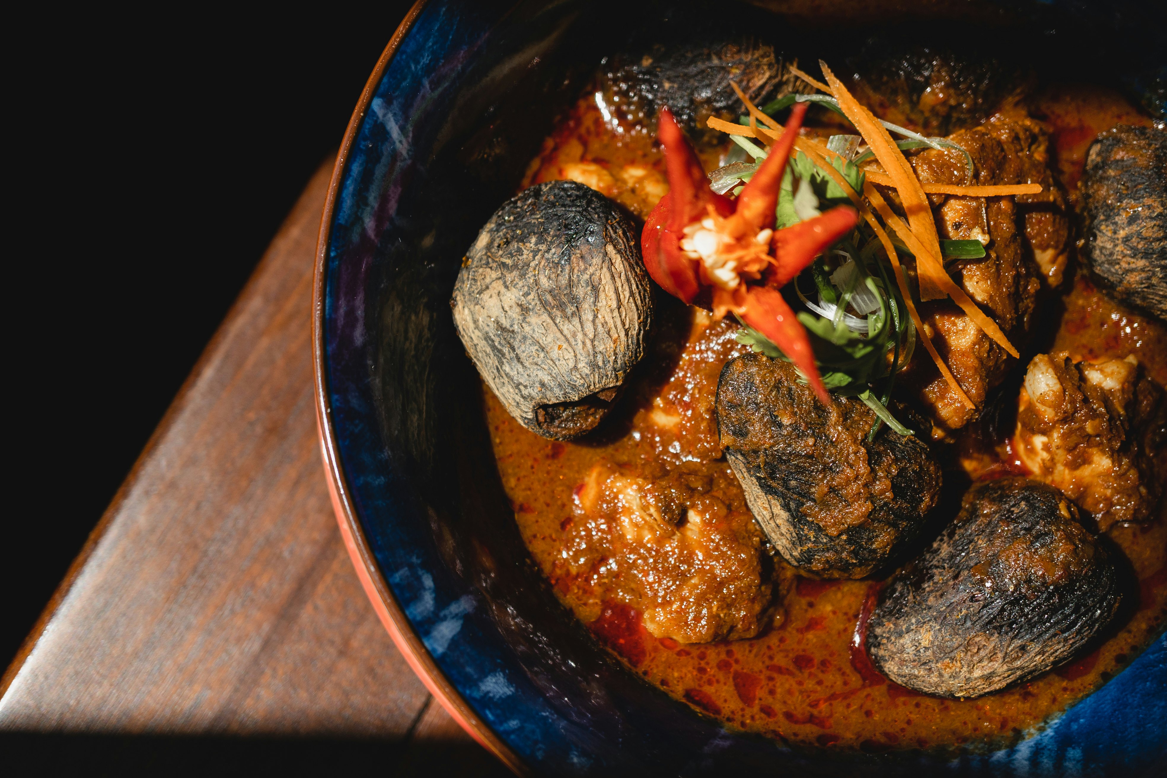 An overhead shot of a dish containing vegetables and other ingredients in a blue bowl on a wooden table.