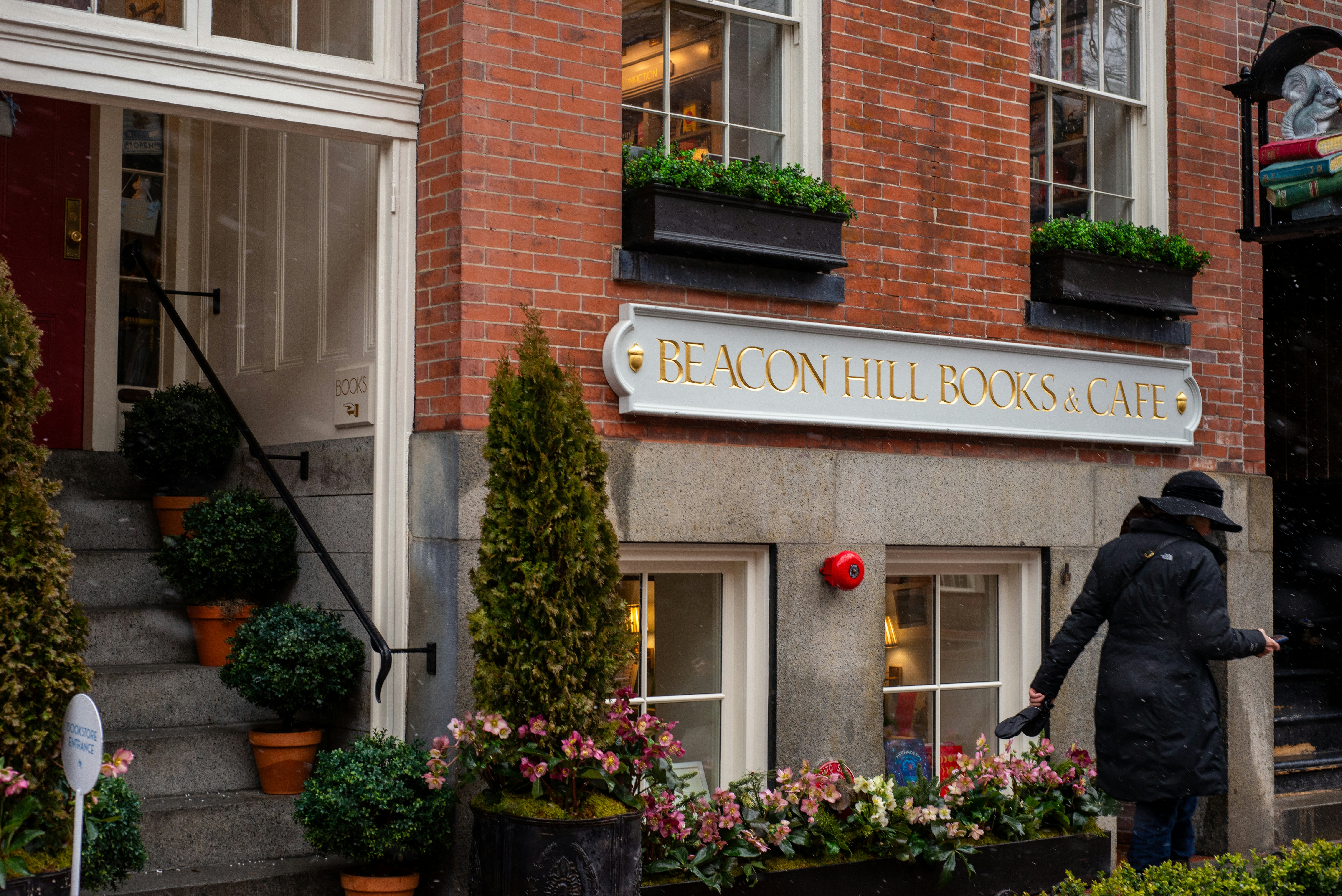 A person exiting Beacon Hill Books & Cafe, with potted plants in the foreground.