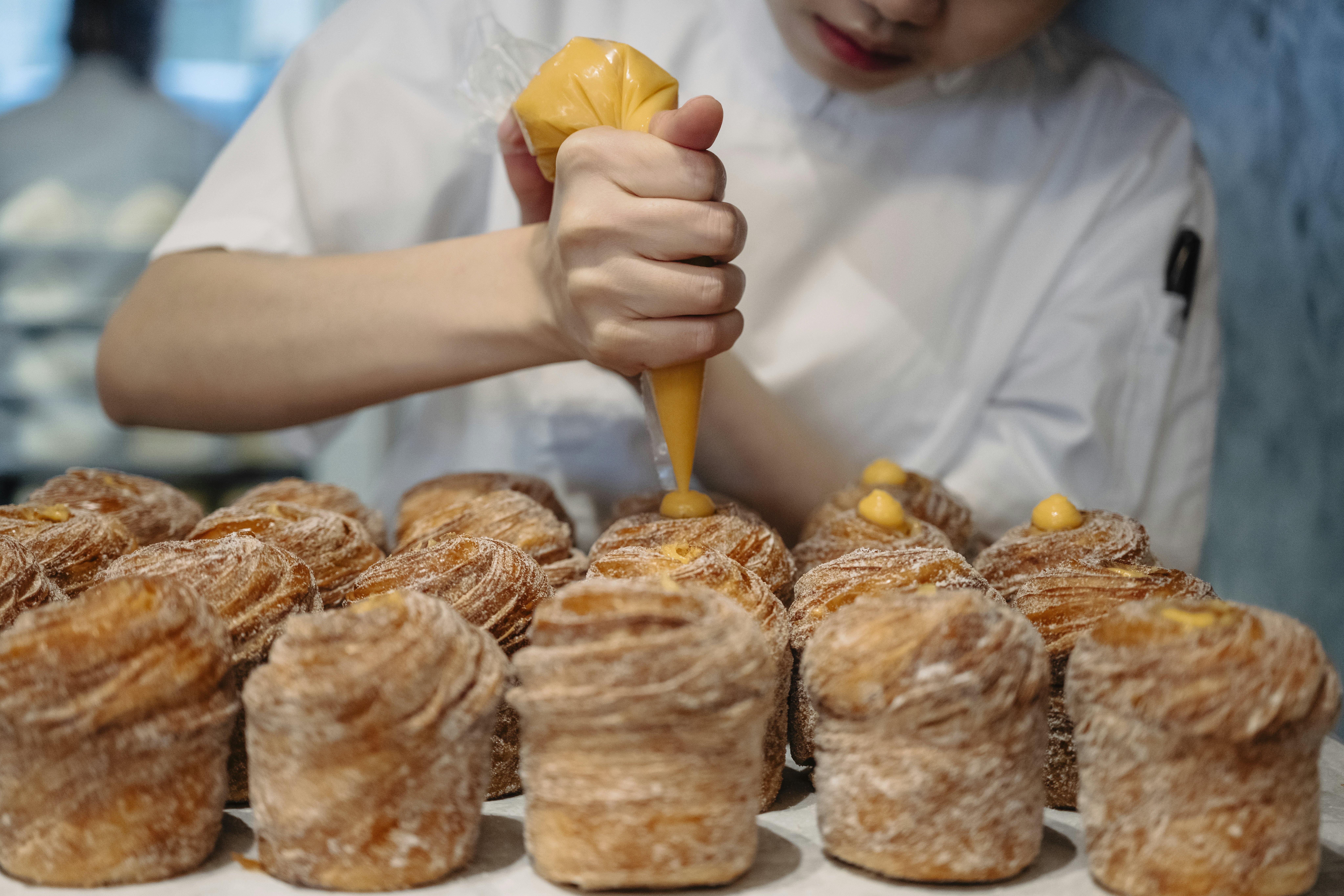 A baker decorates a row of buns with yellow icing in a patisserie.